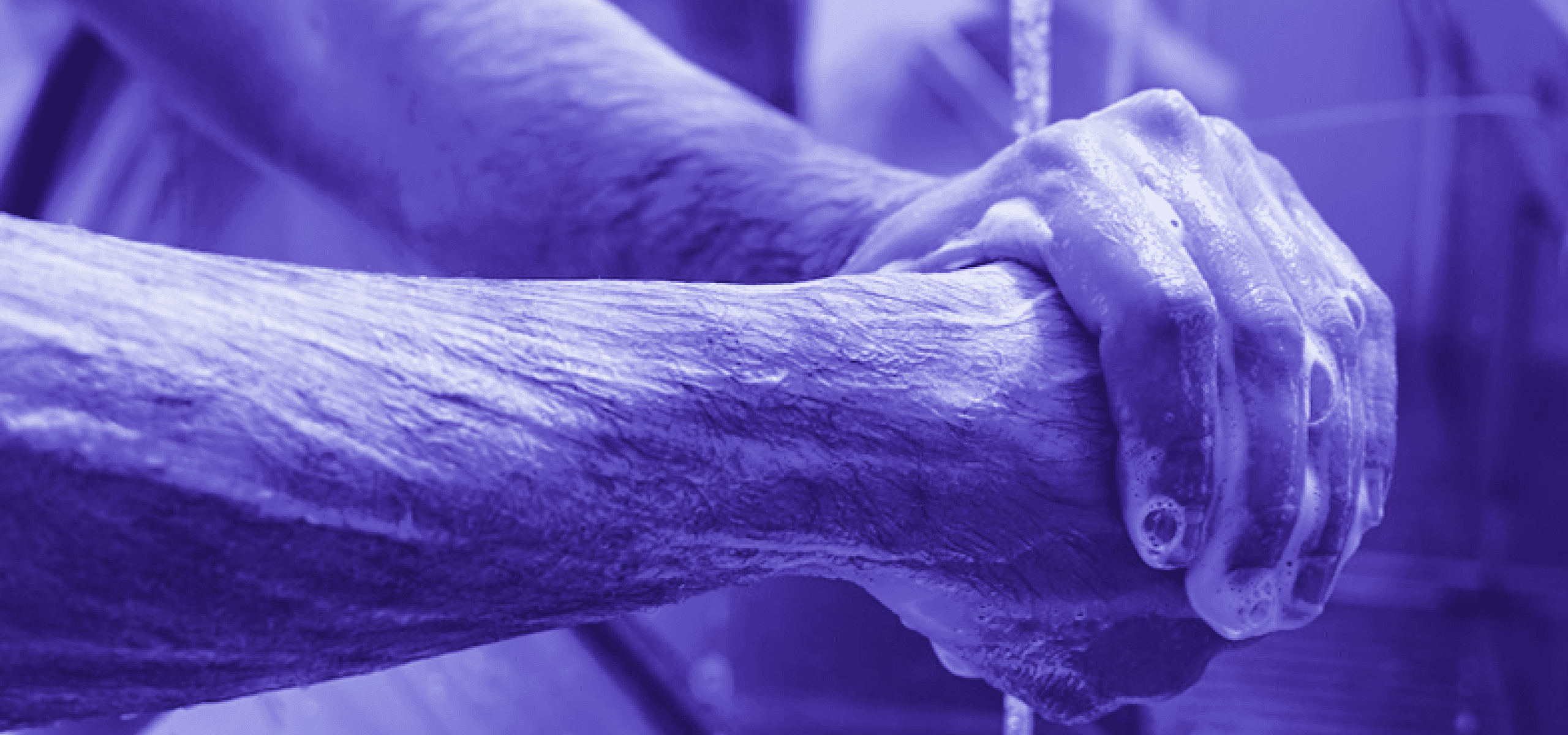 Imagem, em tons de roxo, de um homem lavando as mãos.