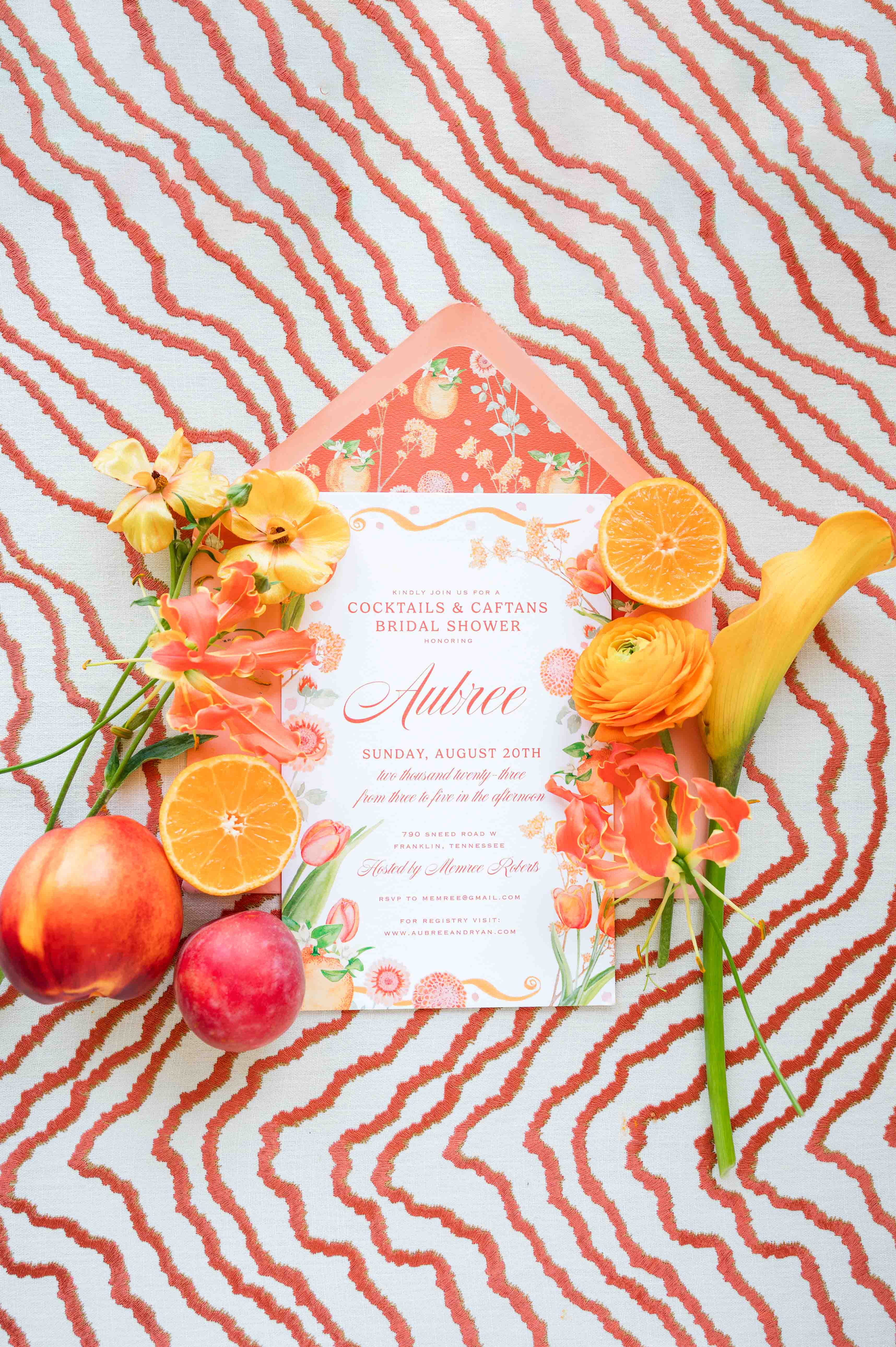 Colorful wedding invitation on a fun orange backdrop with fruit and flowers surrounding it.