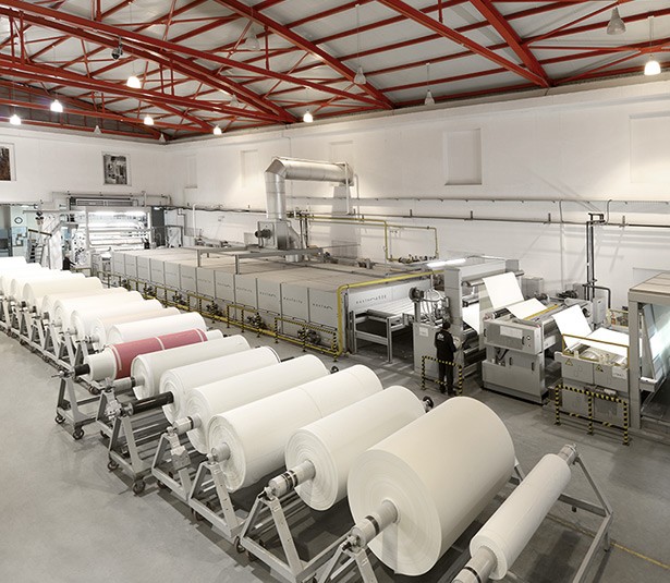 A man and woman sit on beige chairs in a modern room with a red paneled wall. A red pendant light hangs above a wooden coffee table between them.