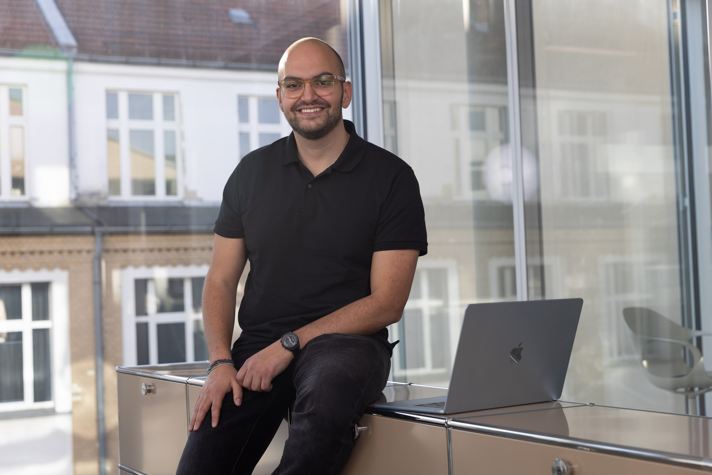 Nabil el Berr., CEO von Indicium, sitzt mit einem Laptop im Büro und blickt in die Kamera und lächelt.
