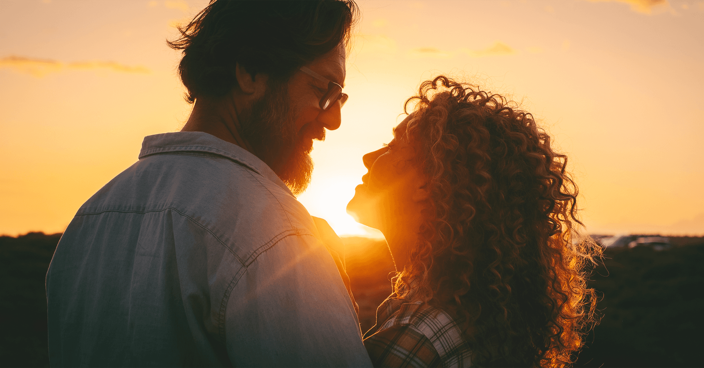 En man och en kvinna tittar djupt in i varandras ögon och ler mot varandra medan de njuter av en vacker solnedgång.