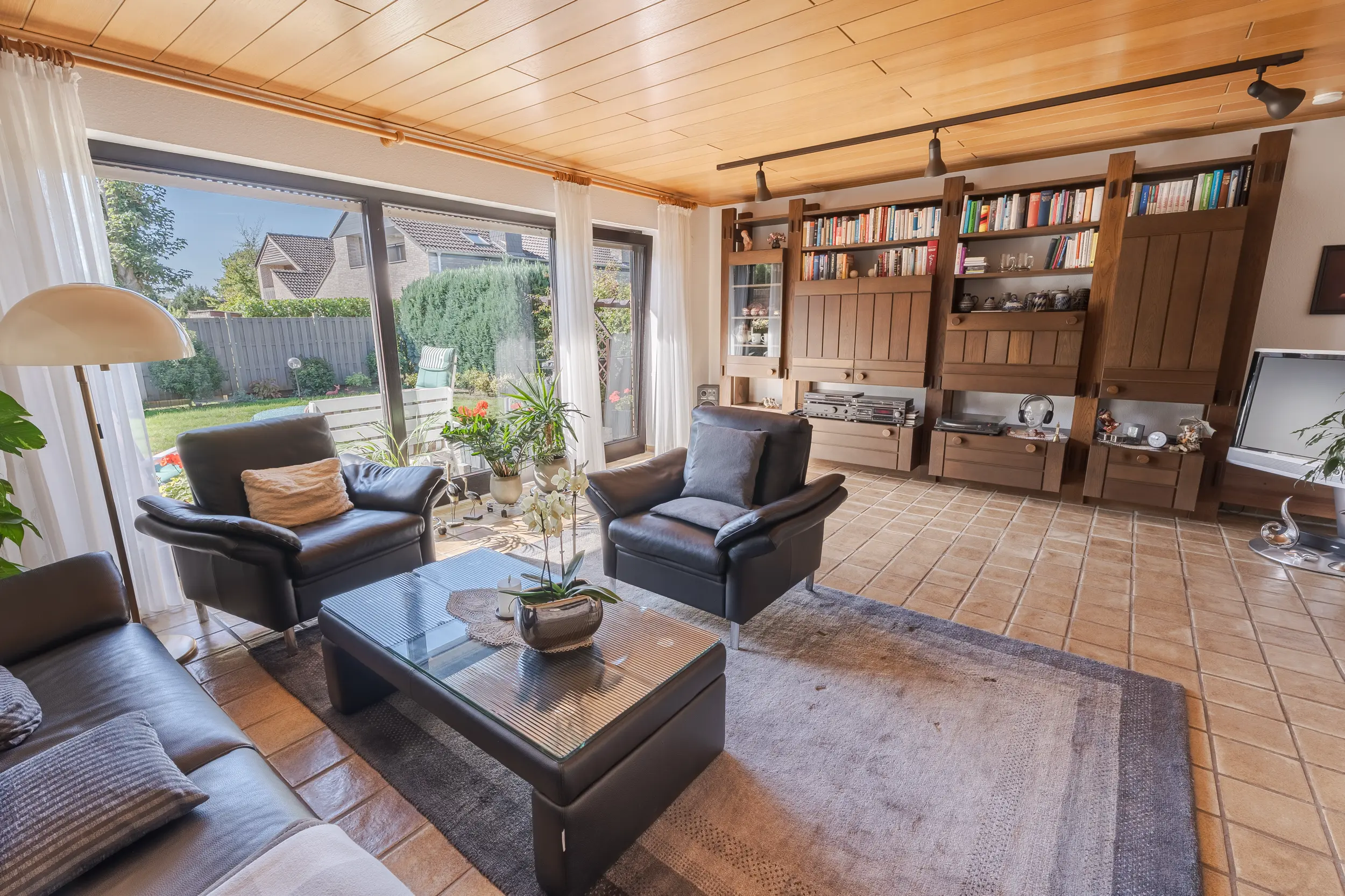 Wohnzimmer der Doppelhaushälfte in Gronau mit großer Fensterfront zum Garten, Holzdecke und gefliestem Boden