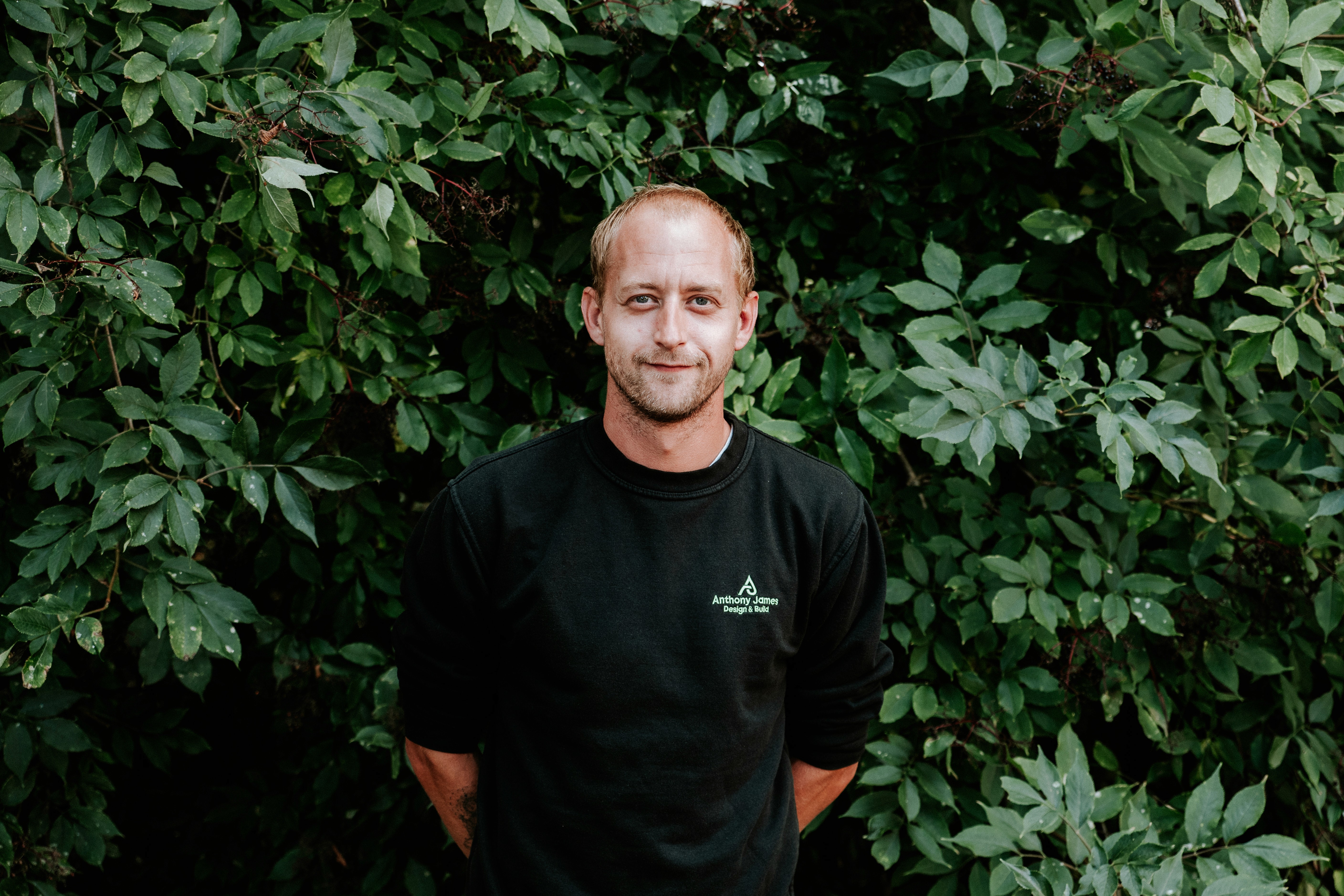 Mature man with glasses and a trimmed beard smiling confidently, standing in warm natural light against a modern backdrop.