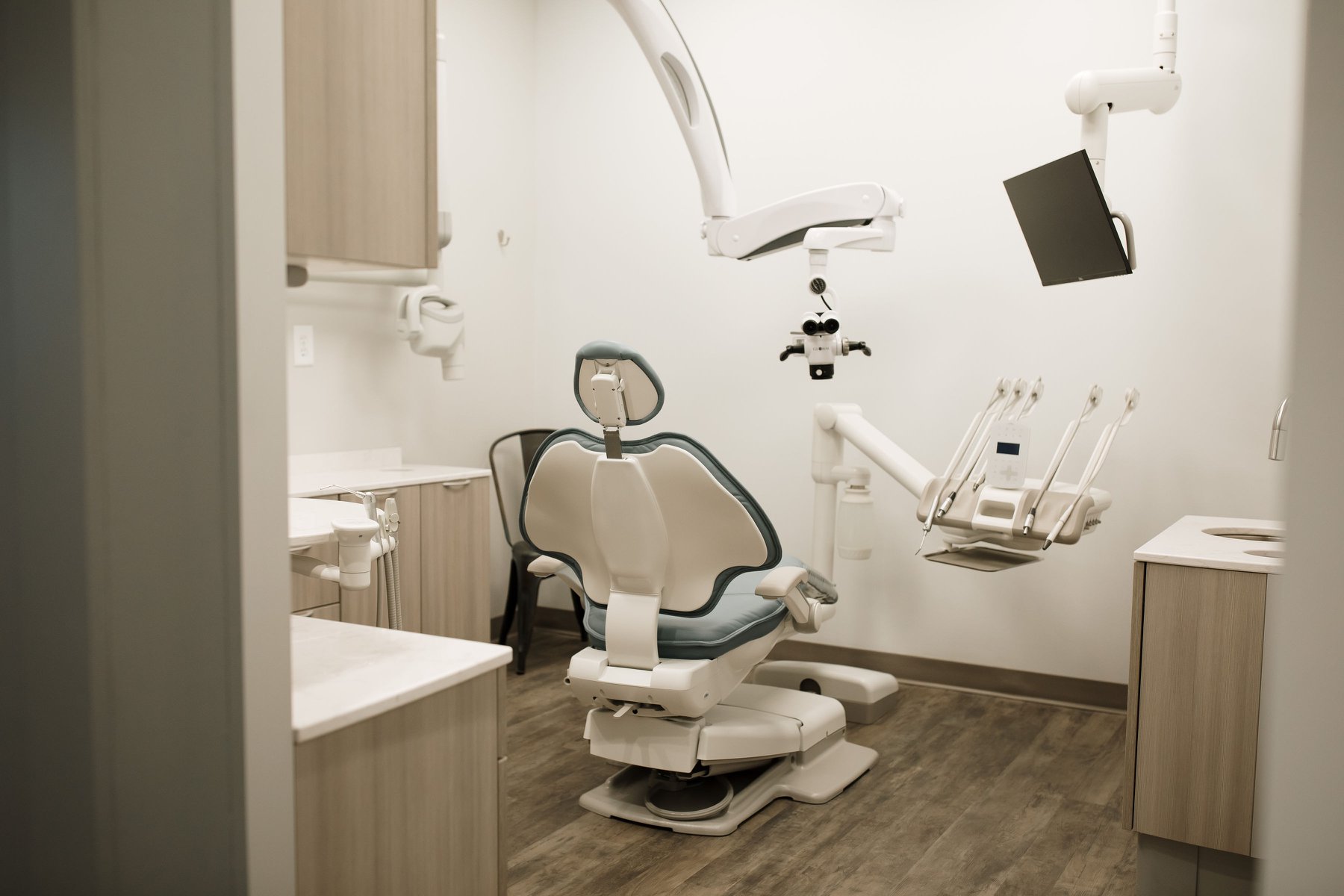 A dentist's office featuring a dental chair, equipment, and minimalistic decor in soft tones.