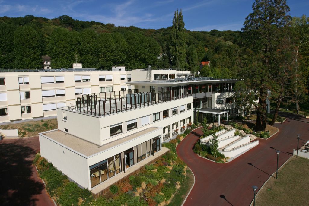 Modern psychiatric clinic with white architecture, manicured gardens, tree-lined landscape, and contemporary facility design