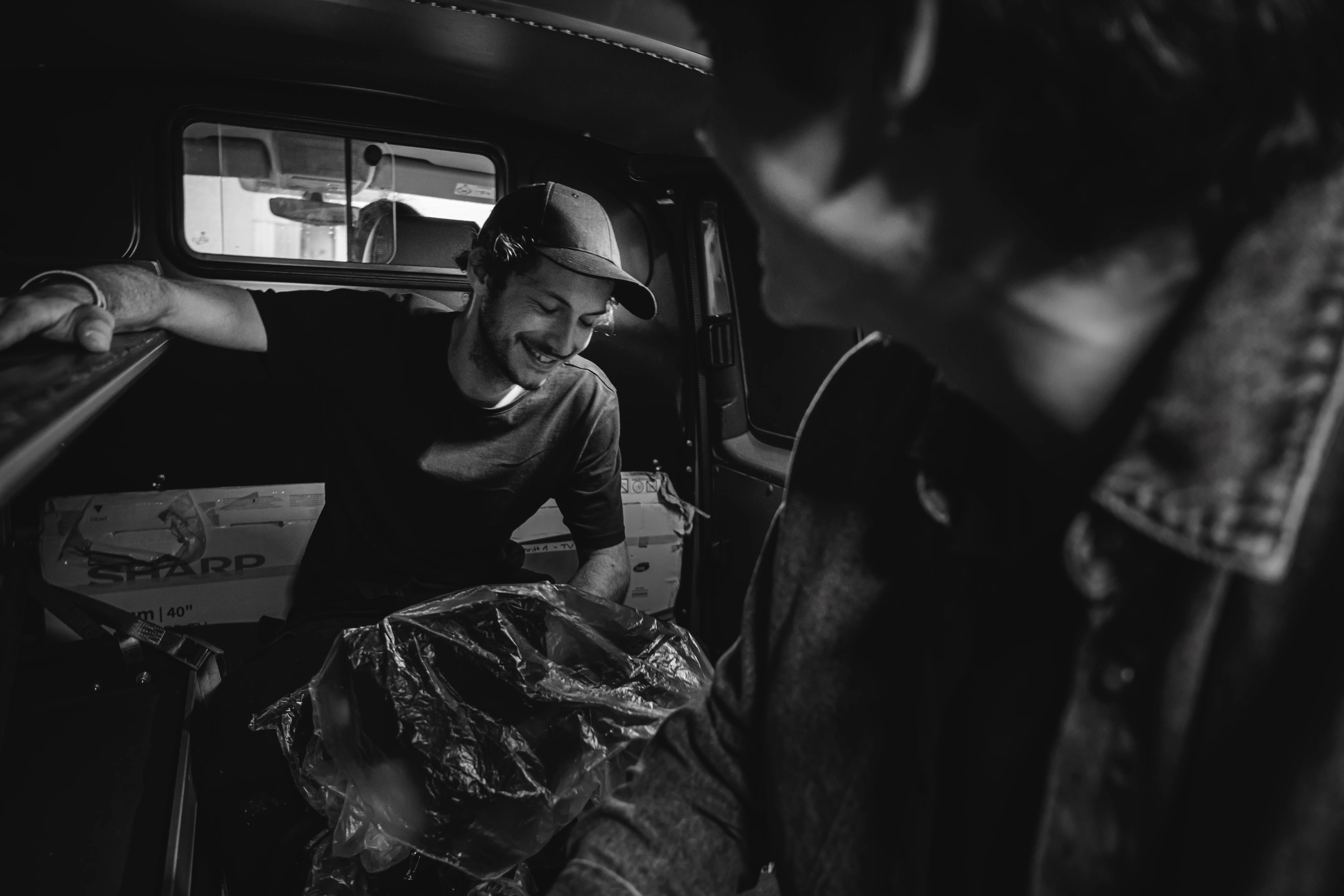 Black and white candid of Director of Photography Morris Schmid smiling while prepping camera equipment in a production van.