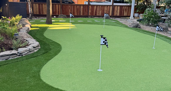 Multi-cup backyard putting green in Sacramento edged by a dry-stack stone wall and a fringe of artificial turf.