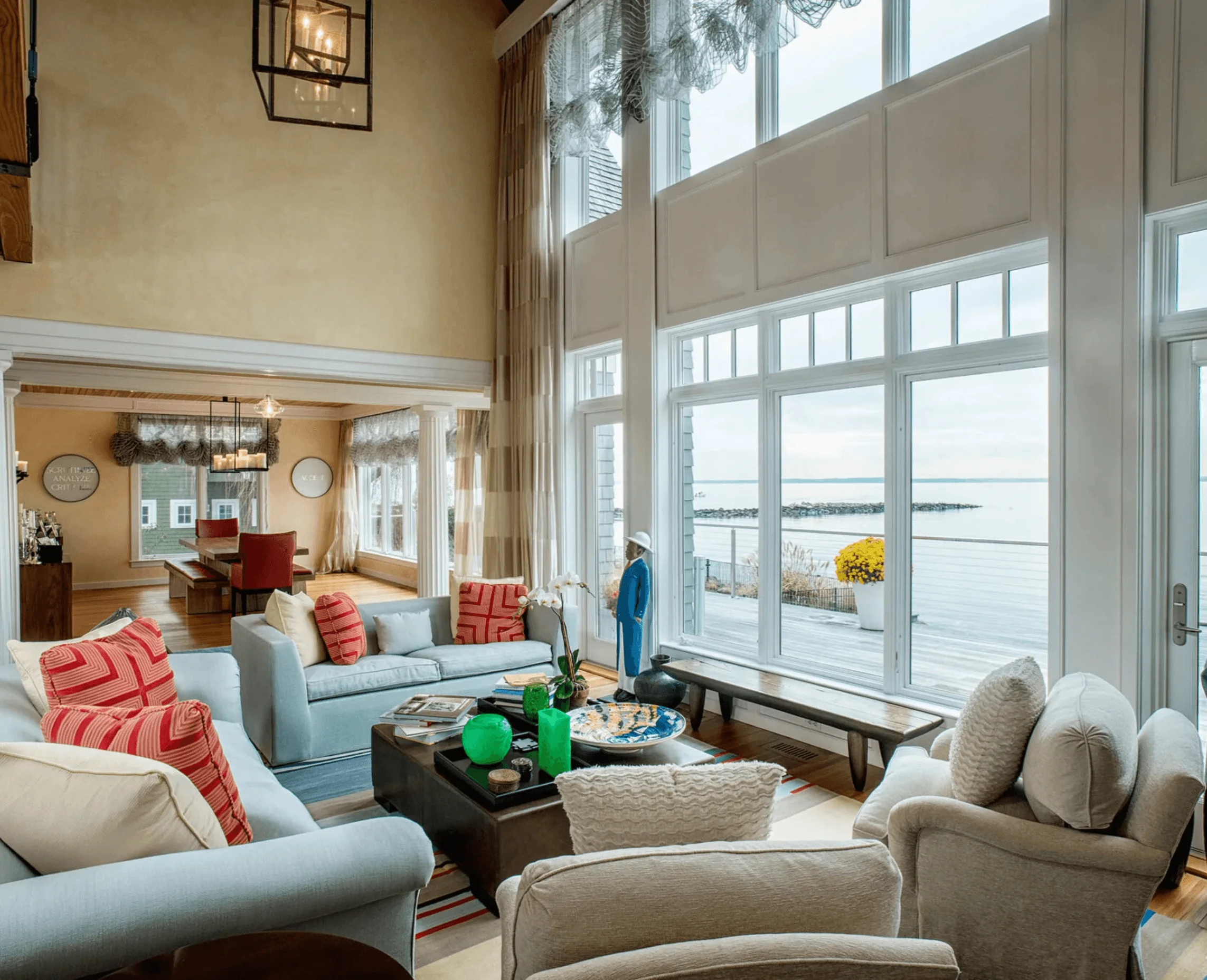 The living room opens to the dining area and a wall of windows overlooking the water, with a wood bench on the deck beyond