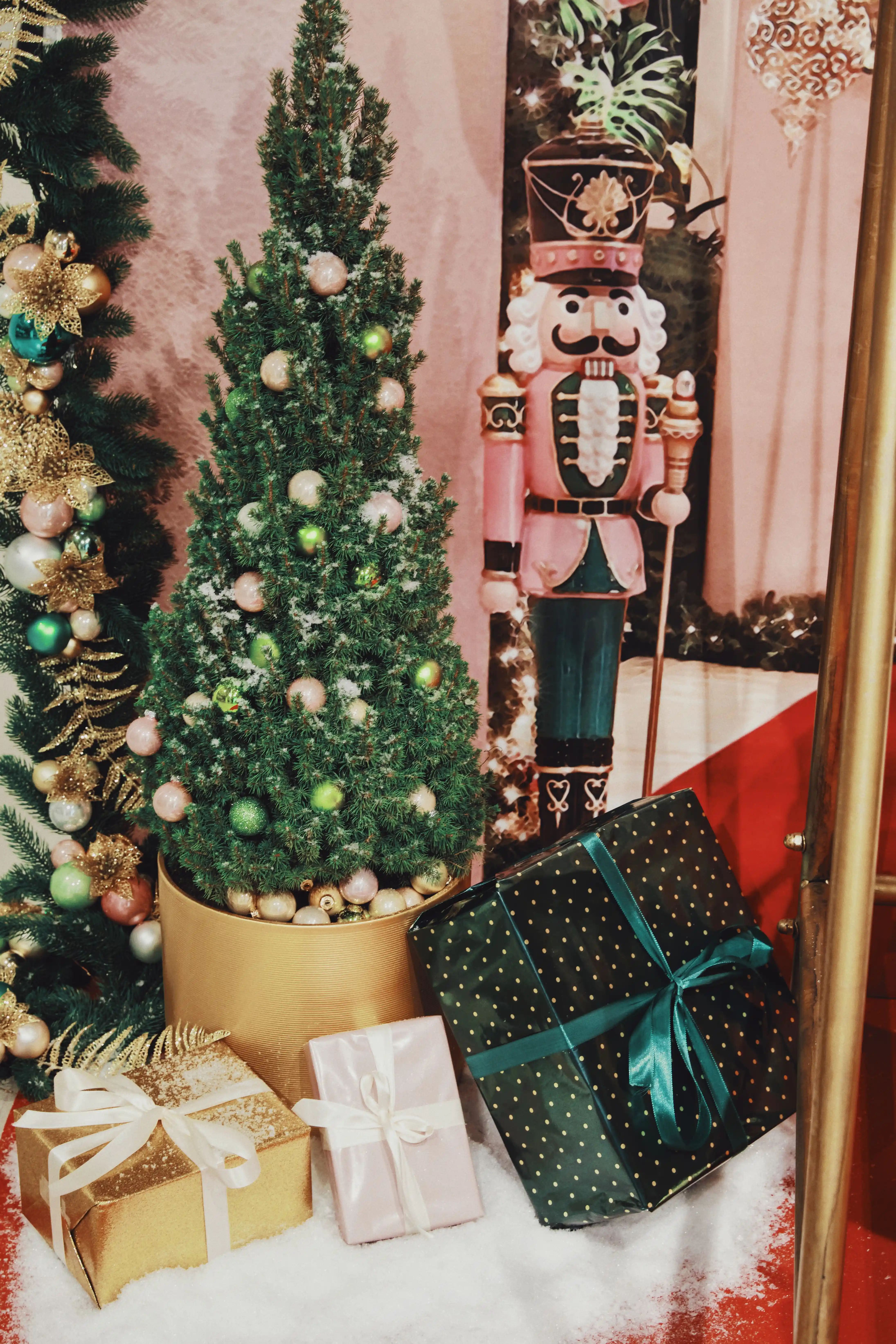 Christmas decoration detail at UZWEI with a small tree with pink and green baubles in a gold pot, wrapped gifts on artificial snow and a life-size pink nutcracker figure.