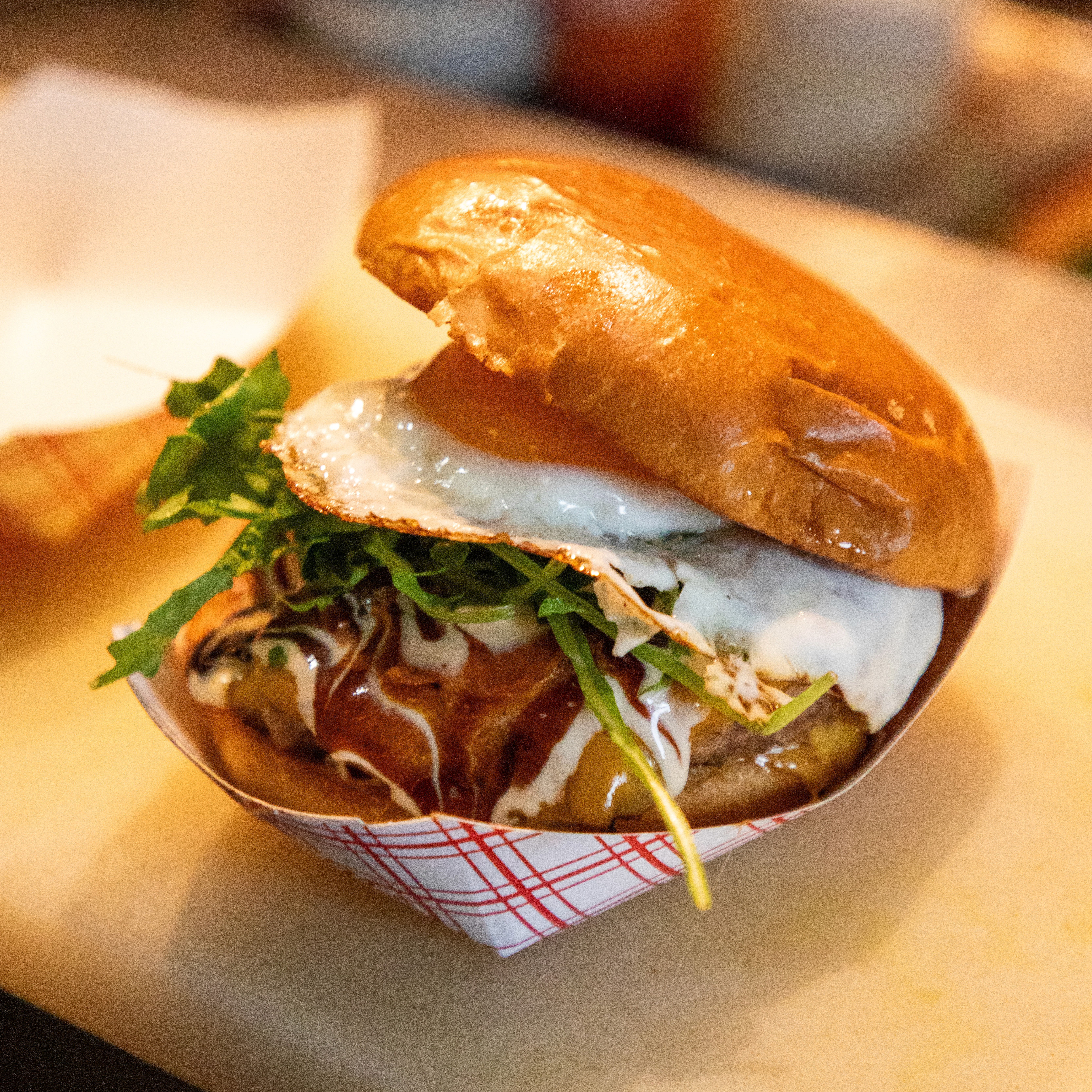 An overhead shot of Patatas Bravas or seasoned roasted potatoes, drizzled with a creamy white aioli sauce and sprinkled with chives, served on a dark gray plate alongside a small bowl of spicy red sauce.