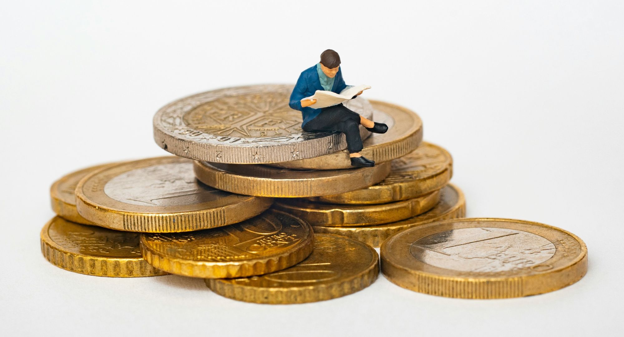 um boneco em minuatura lendo um livro sentado em uma pequena pilha de moedas