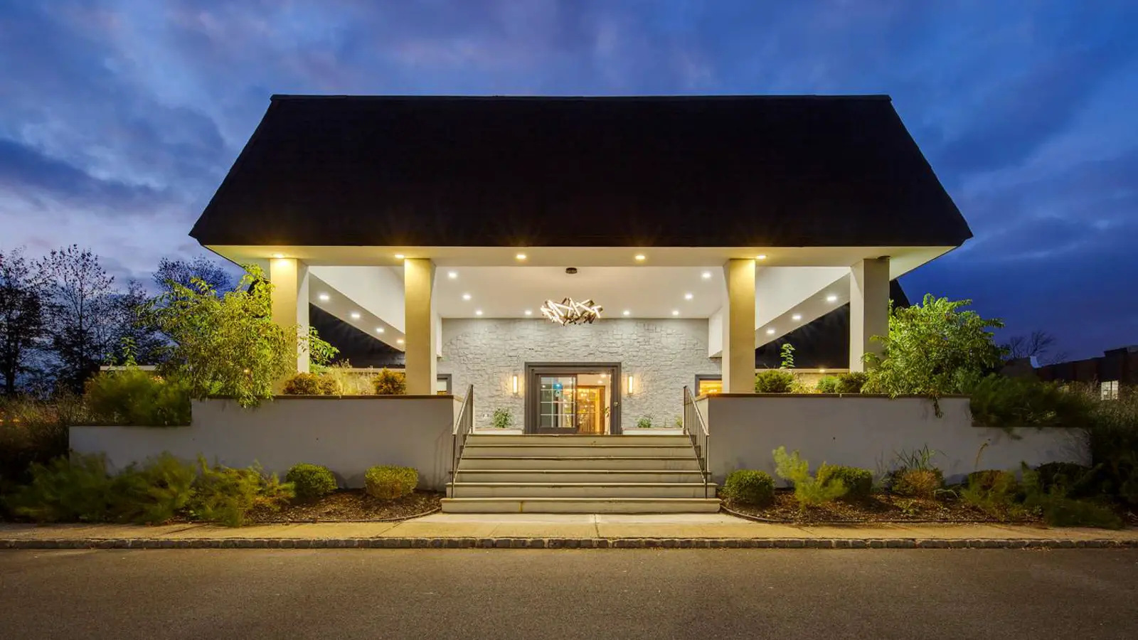 Modern building entrance with a dark roof and bright lights at dusk.