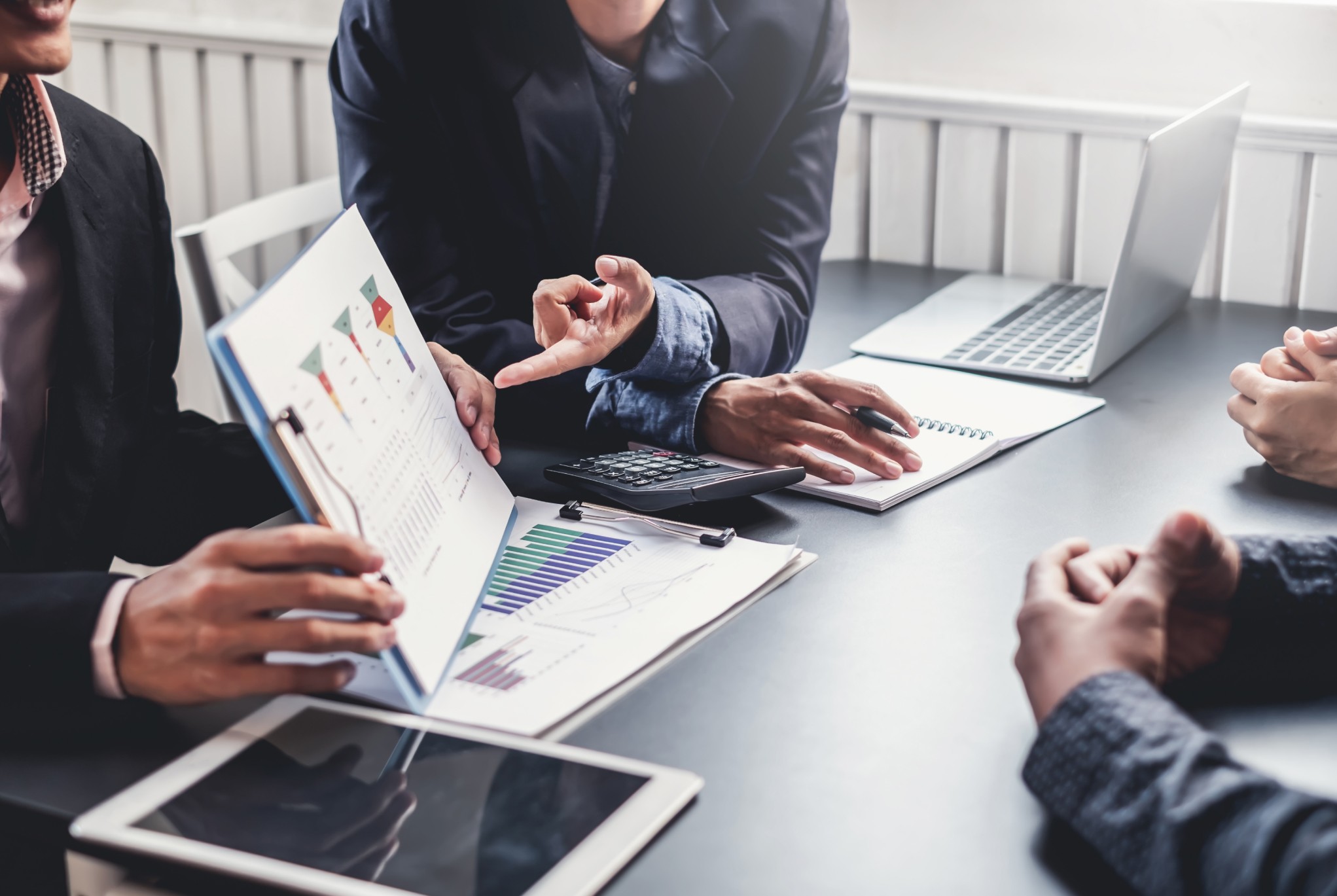 A team of professionals discussing financial charts and graphs in a meeting, with a focus on documents, a calculator, and laptops on the table.