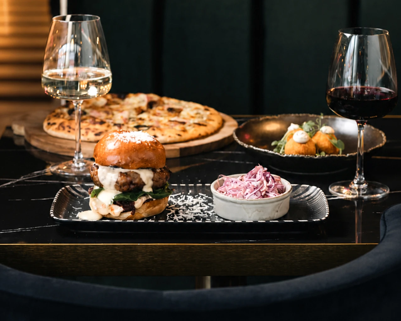 Burger, pizza, appetizers, coleslaw, and wine on a table.