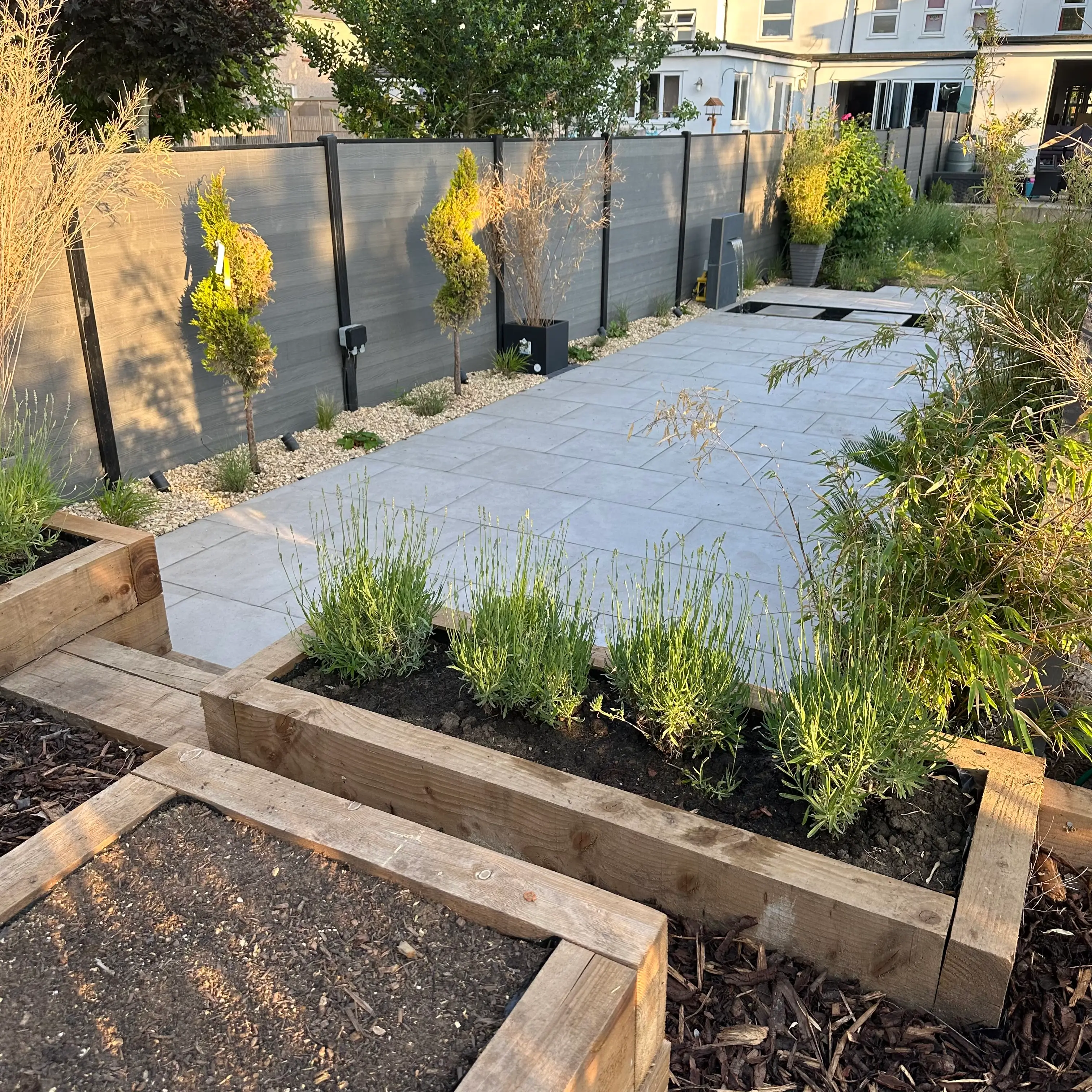 A garden with raised beds, lush green plants, and a covered area for planting, surrounded by a fence.