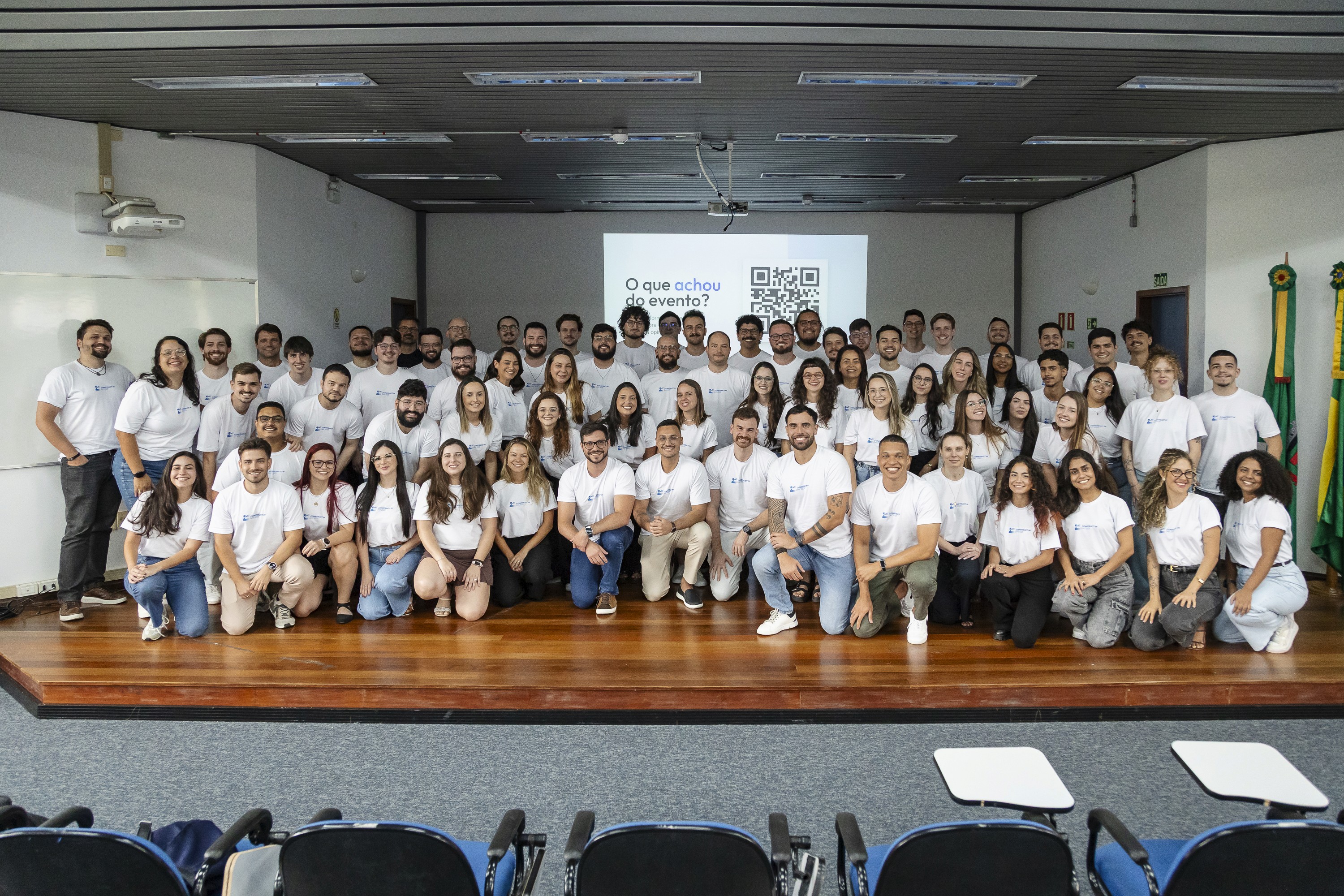 Colaboradores da Construct IN em uma sala de treinamento, durante um evento interno. Eles estão usando camisetas azuis e aplaudindo. A foto captura a equipe em um momento de interação e aprendizado.