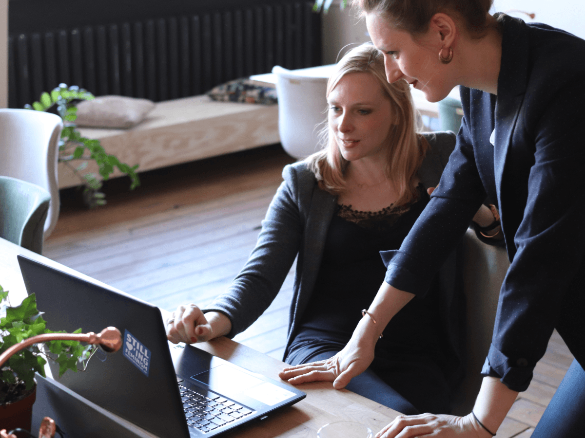 woman in dark blazer working with a colleague on a laptop