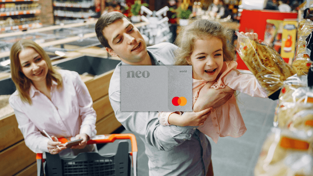 A smiling young newcomer woman sitting at a modern cafe table in Canada, holding a dark Neo Financial credit card and checking her smartphone app. A laptop is open in front of her. The Neo Financial logo is visible in the top right corner. The image highlights the modern, digital banking experience and cashback rewards available to immigrants using products like the Neo World Mastercard.