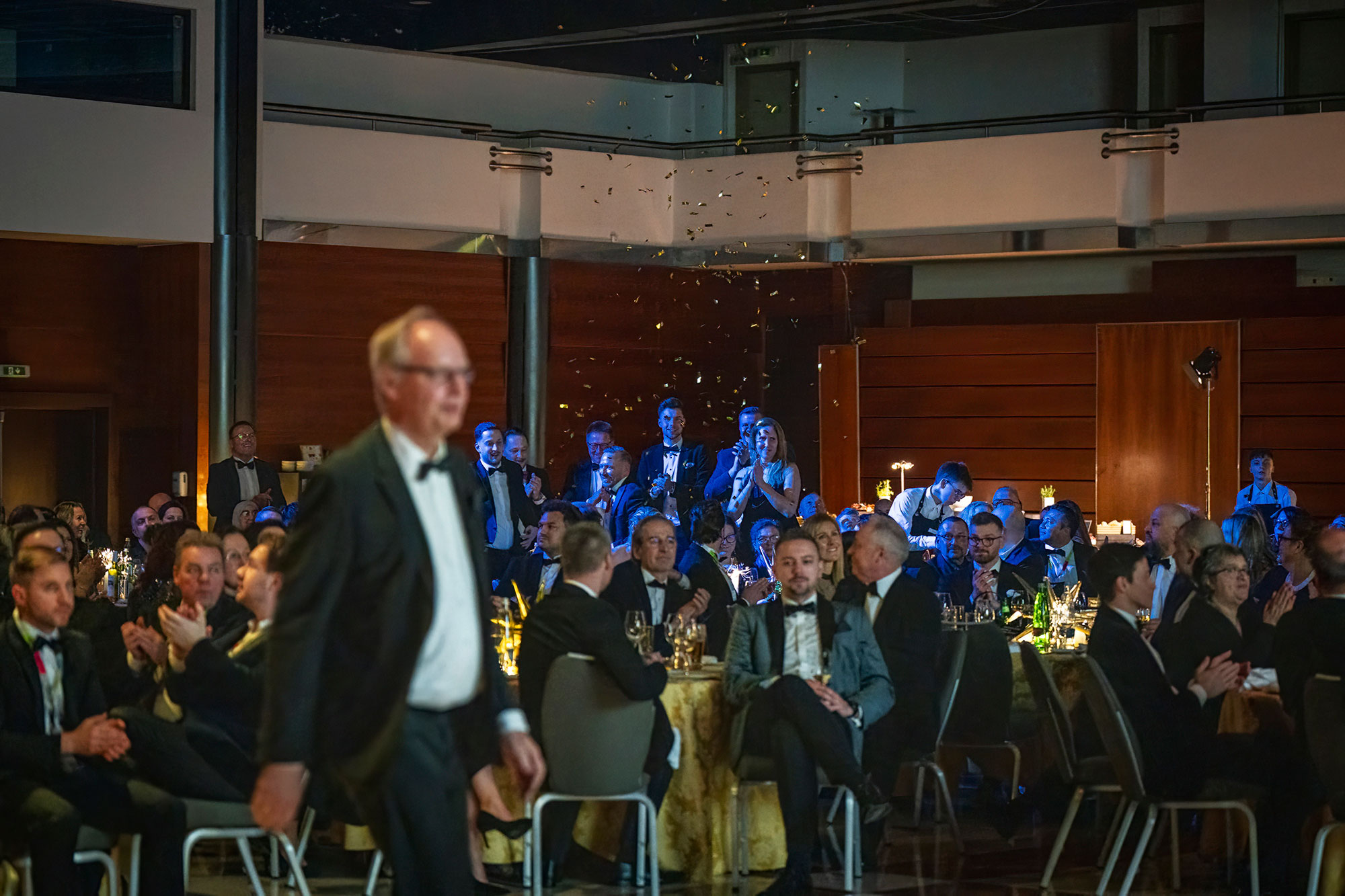 Audience applauding as an award recipient walks through the room during a formal corporate gala evening.