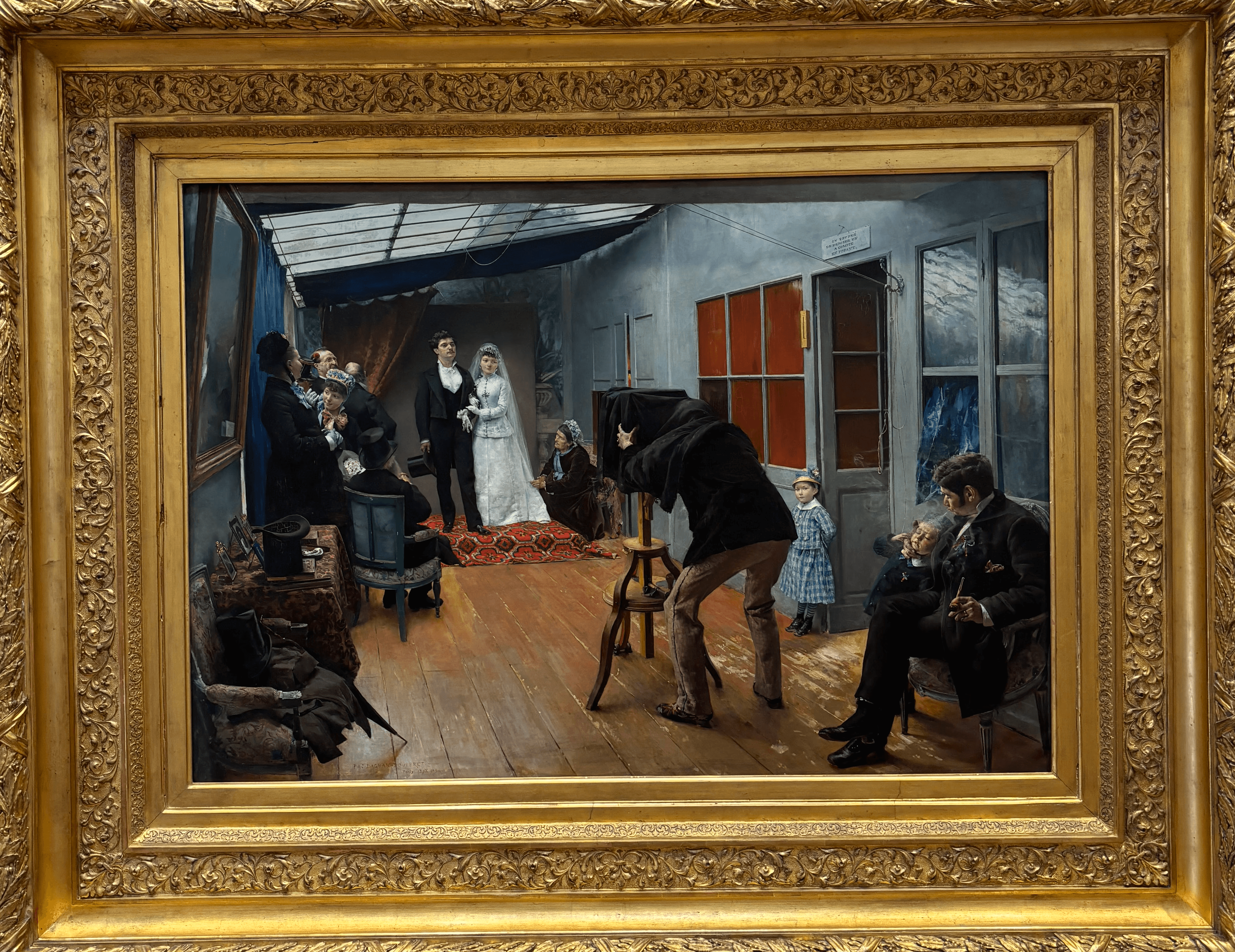 Une noce chez un photographe" de Pascal Dagnan-Bouveret (1879), huile sur toile, dans son cadre doré sculpté, Musée des Beaux-Arts de Lyon. Scène d'intérieur dans un atelier photographique parisien : au centre, les mariés en tenue de noce posent devant l'appareil photo tandis que le photographe, penché sous son drap noir, s'apprête à déclencher. Autour d'eux, la famille et les invités attendent, chacun dans sa propre attitude. Lumière zénithale par verrière, plancher en bois, tons chauds et détails naturalistes très soignés.
