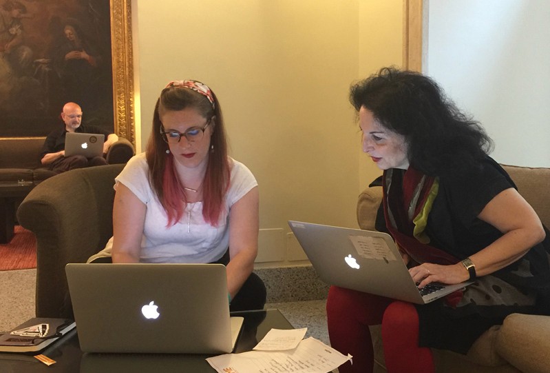 A photo of three people, each looking at their laptops and comparing notes.
