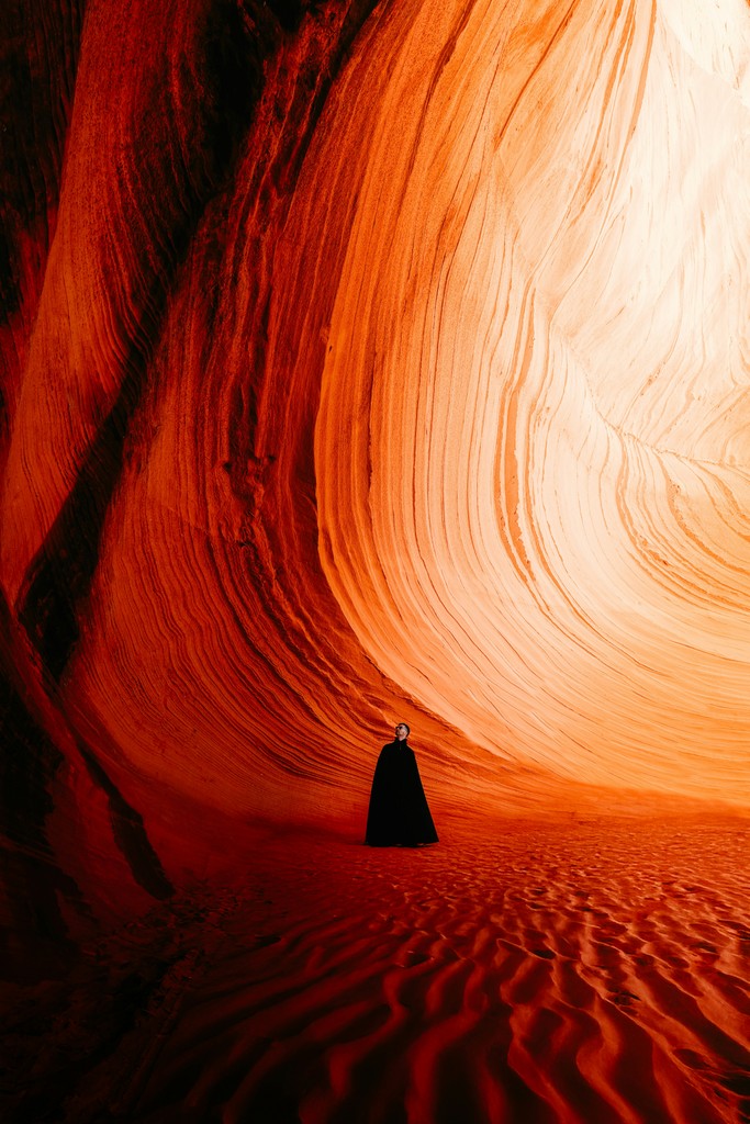 Person in dark cloak stands in glowing orange sandstone canyon