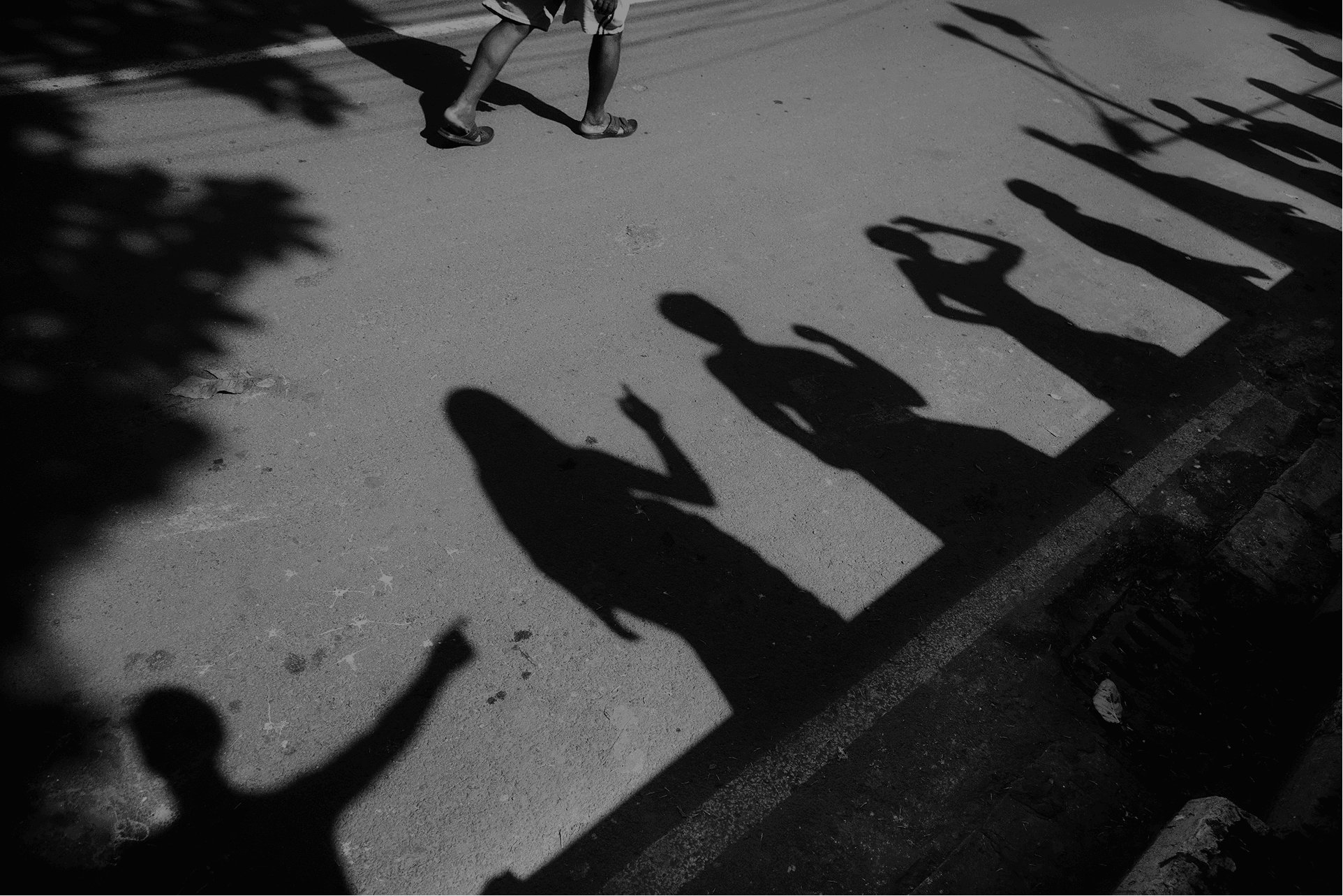 Dramatic black and white shadows of people cast on a sunlit street, creating strong contrast and abstract urban street photography.