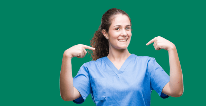 Smiling healthcare worker in scrubs pointing at herself on a green background