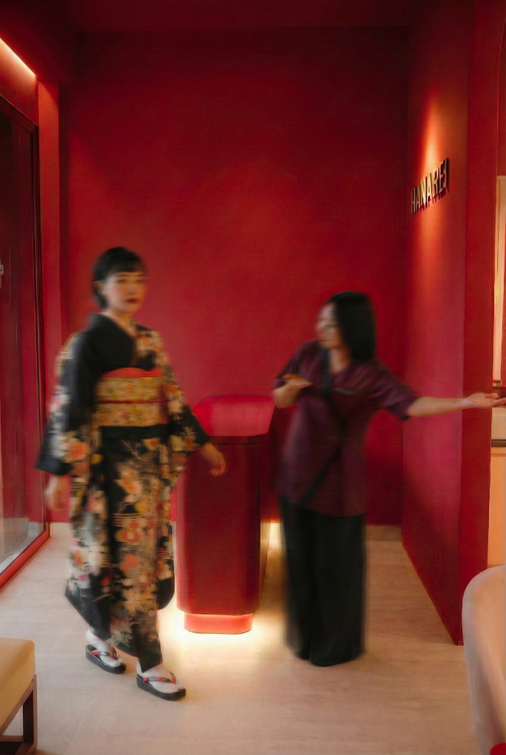 Two women in a red room, one wearing a kimono, the other in a purple top and black pants.