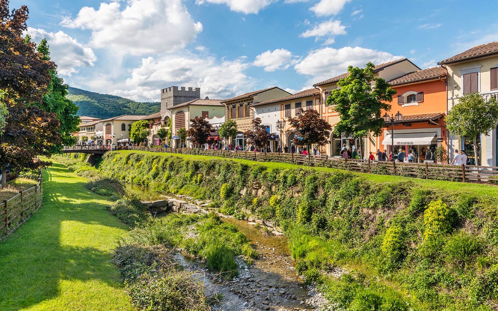 购物者漫步于意大利佛罗伦萨的Barberino名品奥特莱斯，周围环境优美，绿意盎然。
