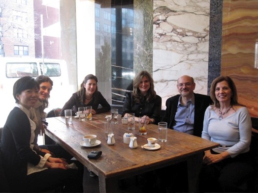 A photo of a group of people sitting at a table with glasses and coffee cups on it.