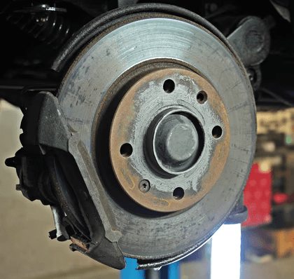Close-up of a vehicle brake disc and caliper in a repair shop.