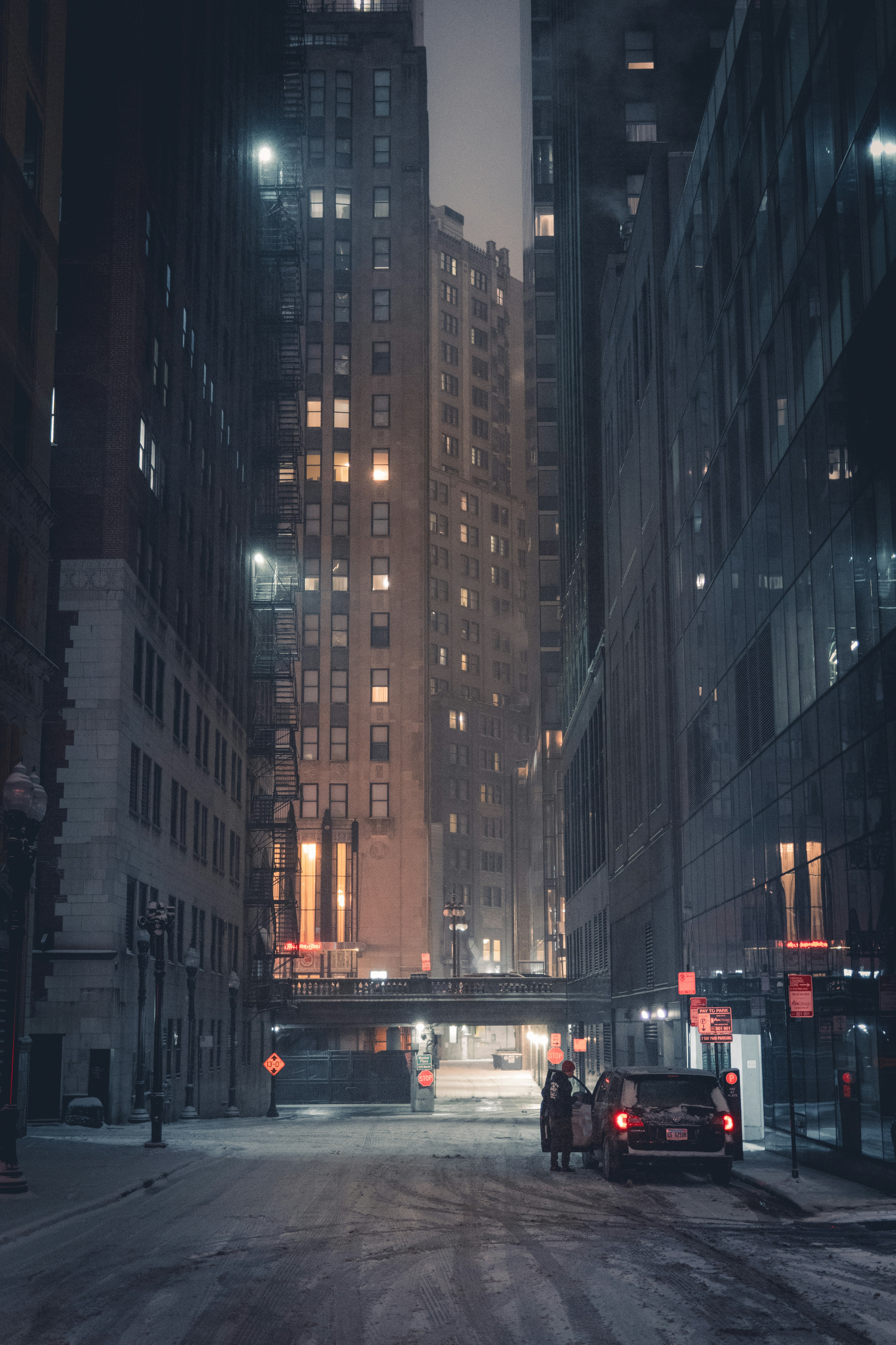 City street at night with tall buildings and car.