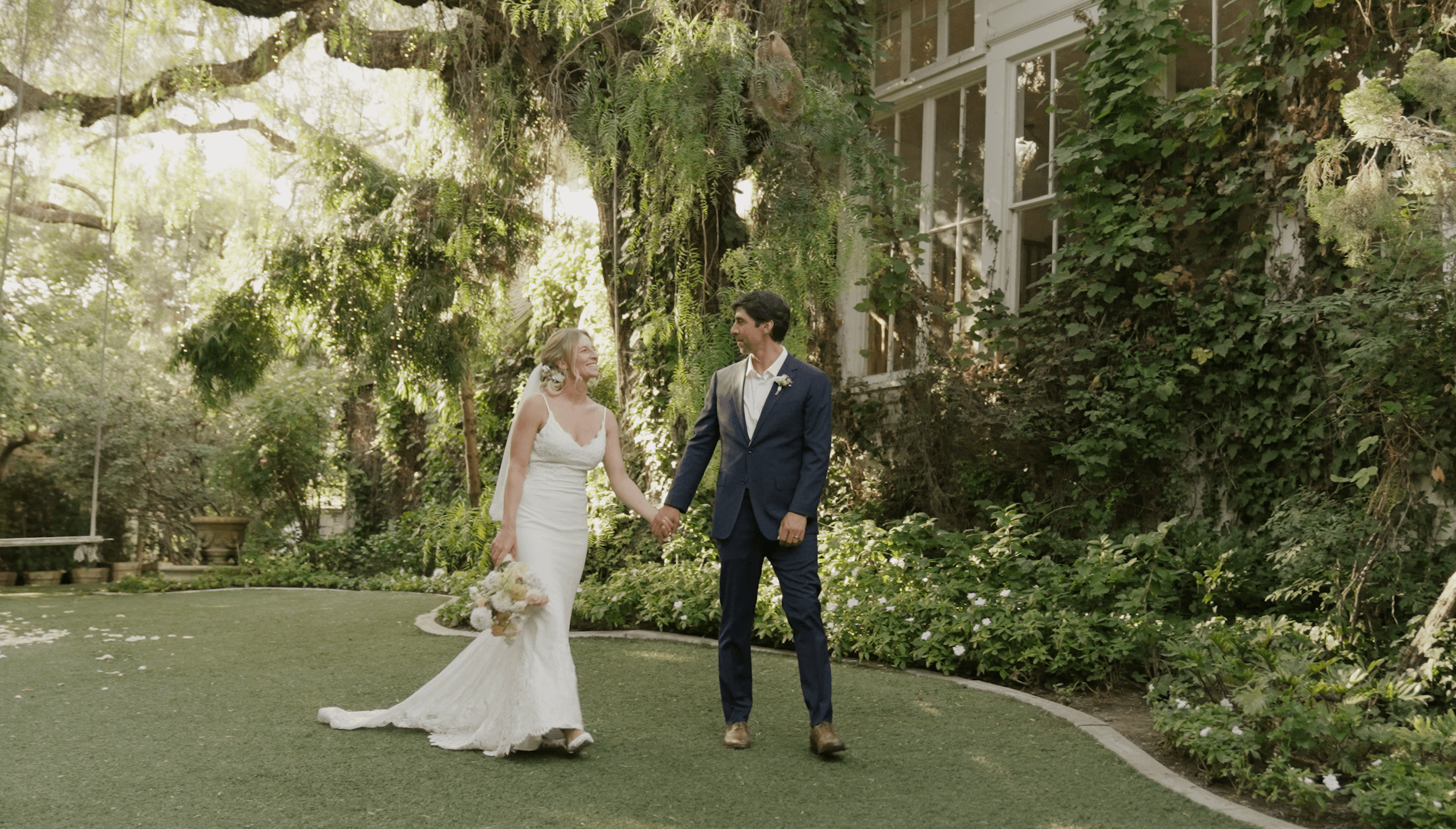 A San Diego bride and groom walk hand in hand in a lush garden setting, surrounded by greenery and elegant decor at the Green Gable in San Marcos, California.