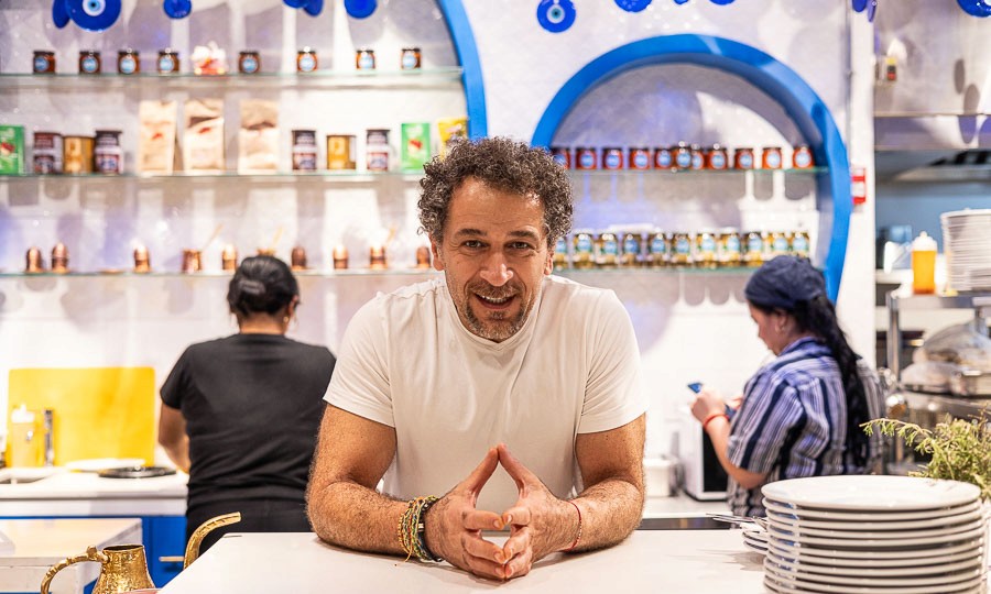 Restaurant interior with wooden tables and chairs lined against a textured wall, softly lit by round wall lamps.