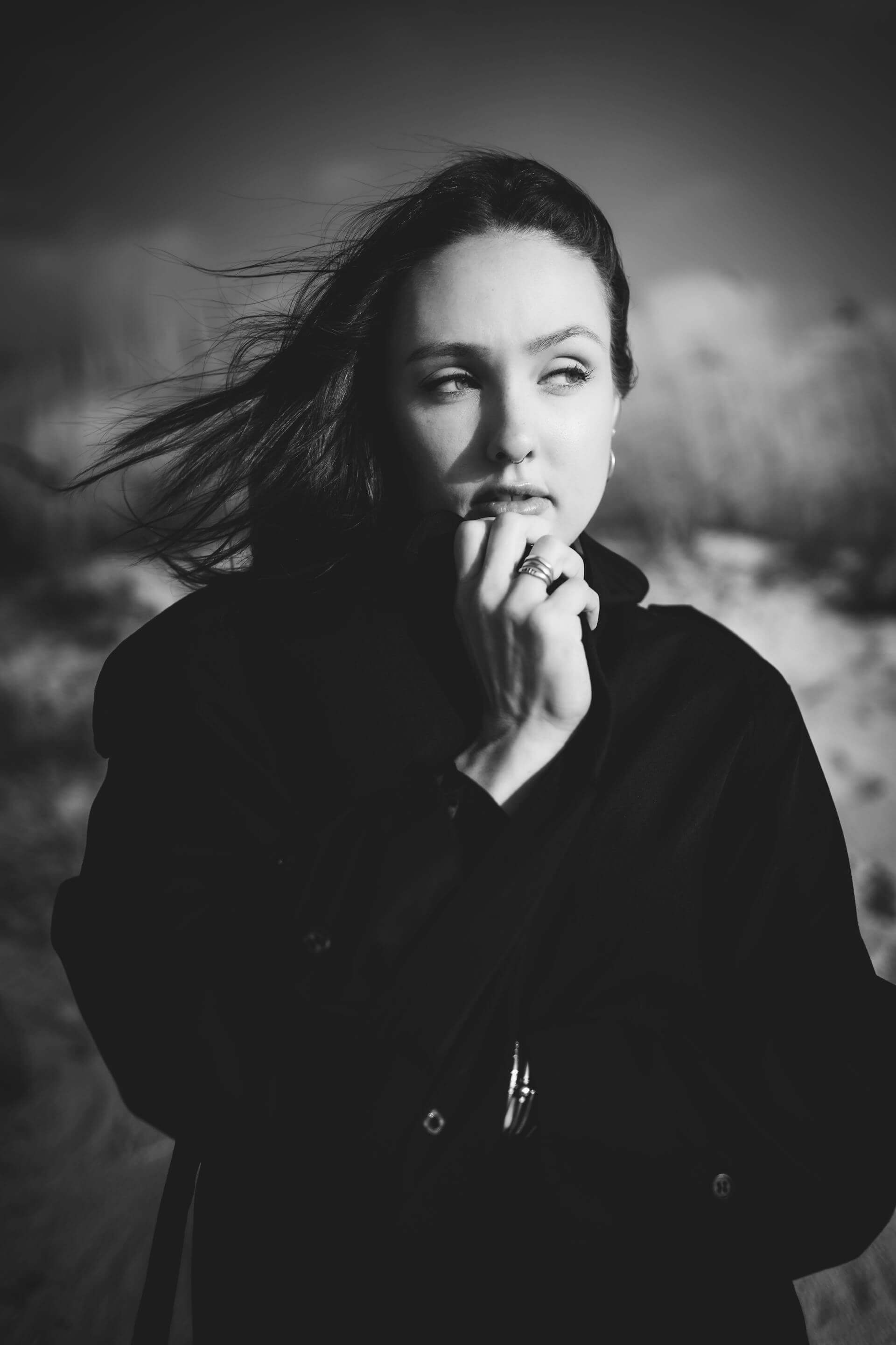 A black and white photo of a woman standing on the beach, gazing at the waves with a serene expression