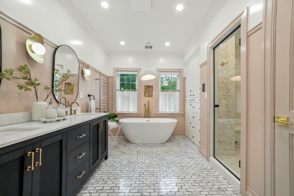 Modern bathroom featuring a walk-in shower, wooden vanity, round mirror, and elegant marble tiles.