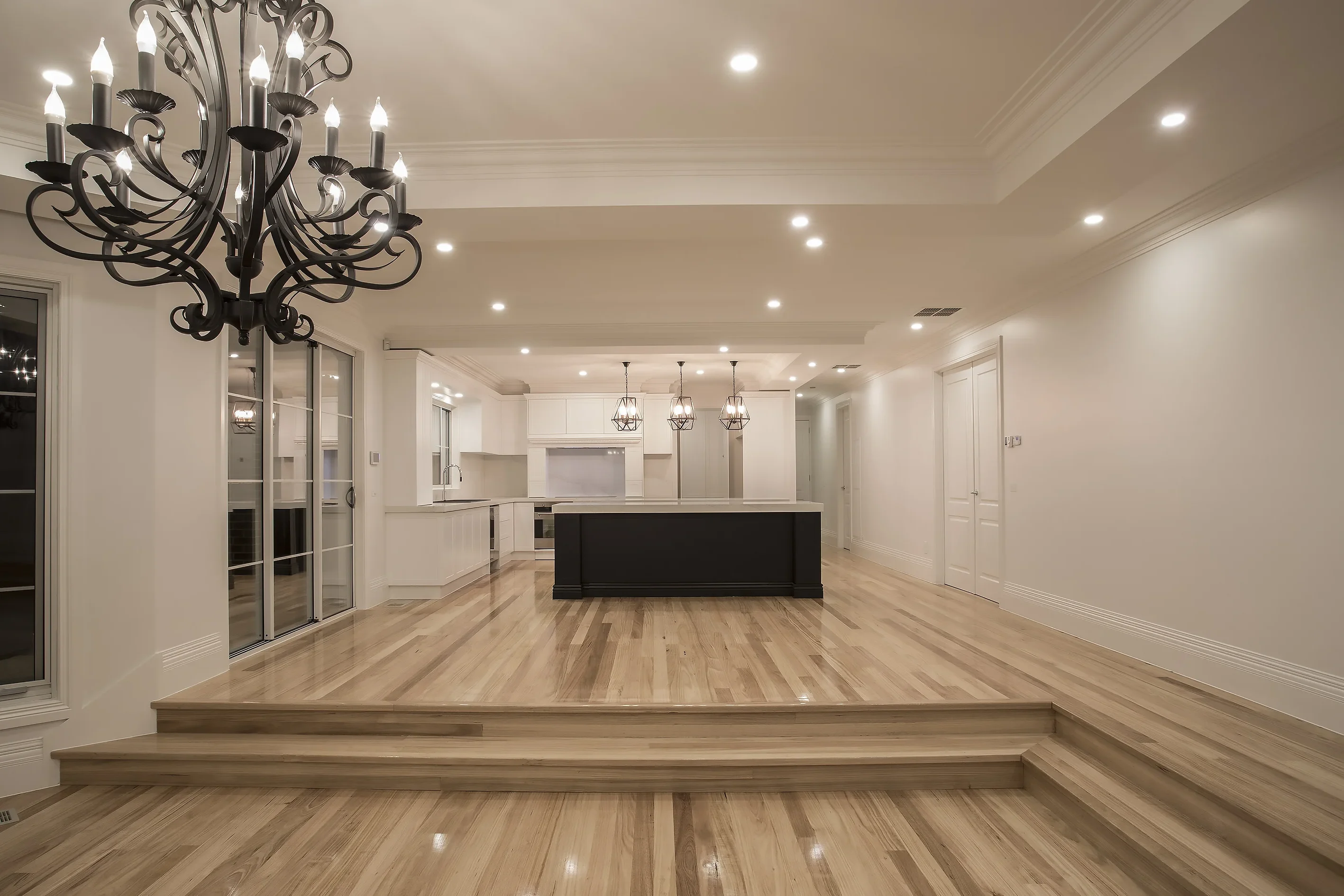 Open-plan living and kitchen area with a black island bench, polished timber floors, wrought-iron chandelier and a stepped floor level