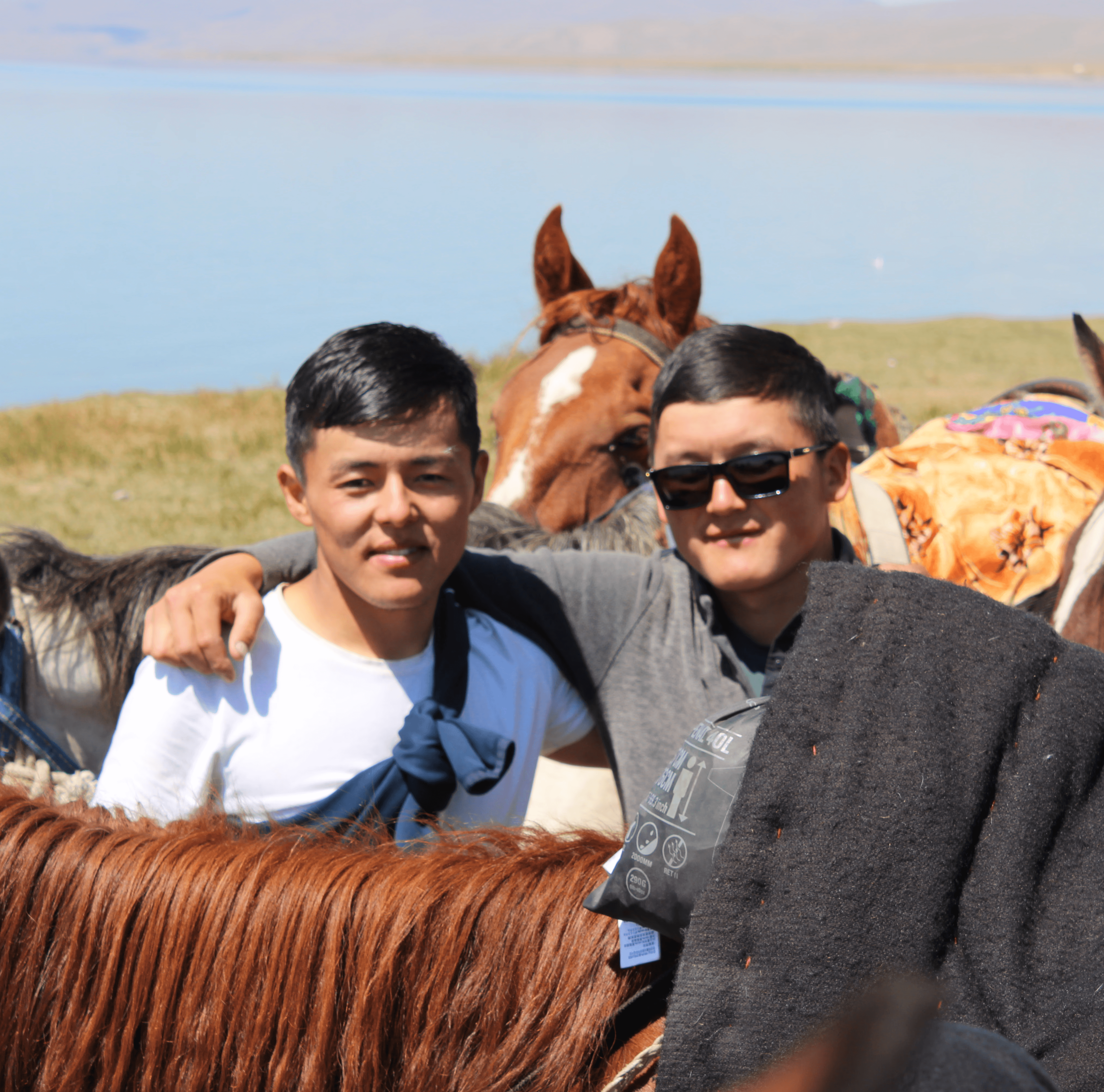 Local Kyrgyz horsemen standing with their horses near a mountain lake in Kyrgyzstan