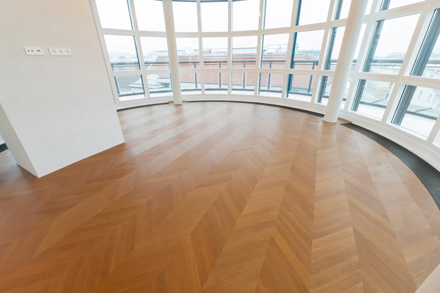 Heller Wohnraum mit gebogener Fensterfront und hochwertigem Fischgrät-Parkettboden.