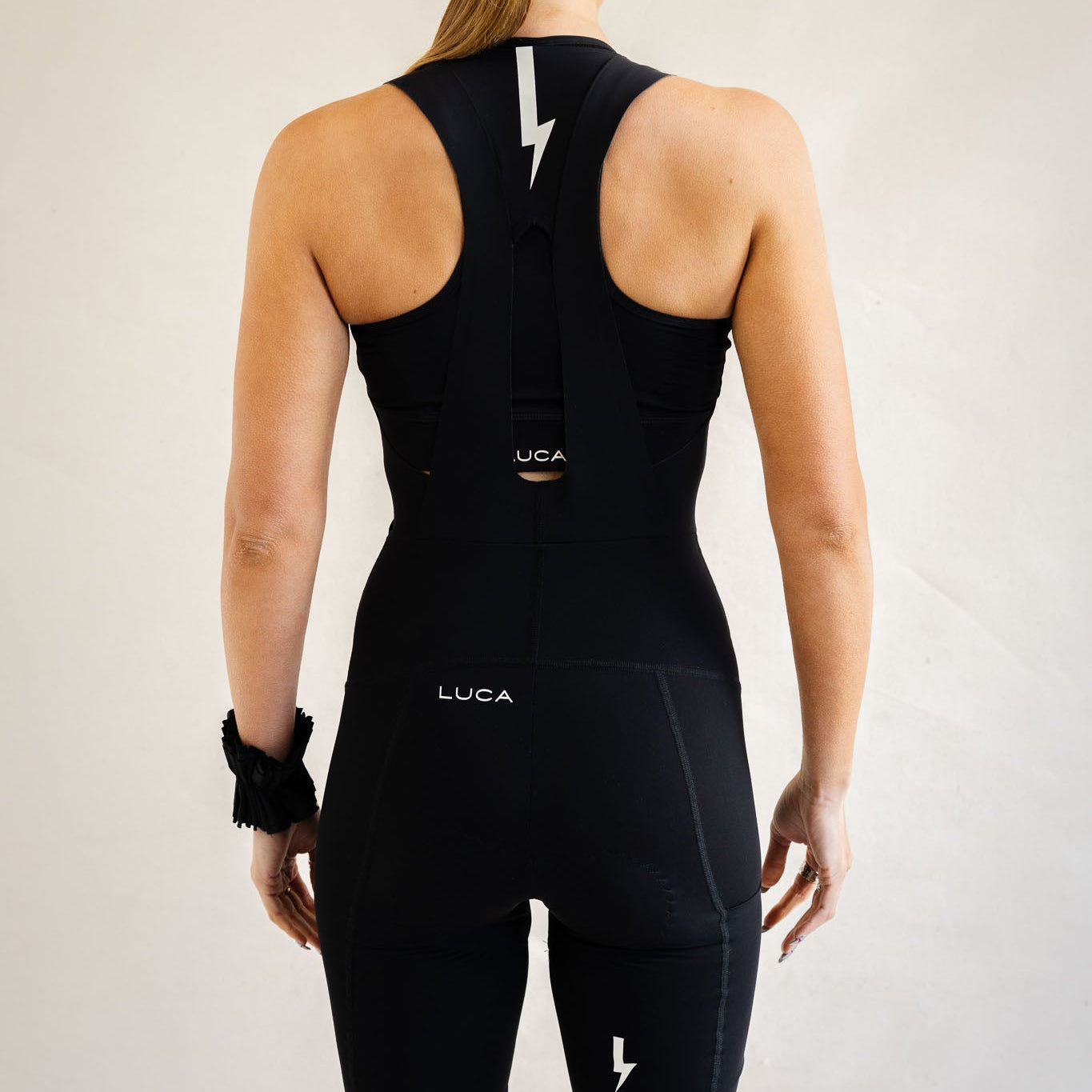 Cyclist wearing LUCA Road All-In-One Cargo bib shorts in black, back view with racerback opening