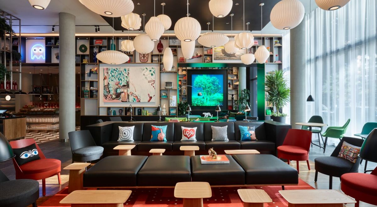 A contemporary hotel lounge featuring colorful seating, a stylish black leather couch, and a modern bookcase beautifully decorated with art and artifacts.