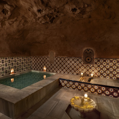 Raskošna prostorija s popločanim zidovima nudi mali, osvijetljeni bazen okružen svijećama i upečatljivim arhitektonskim lukom.