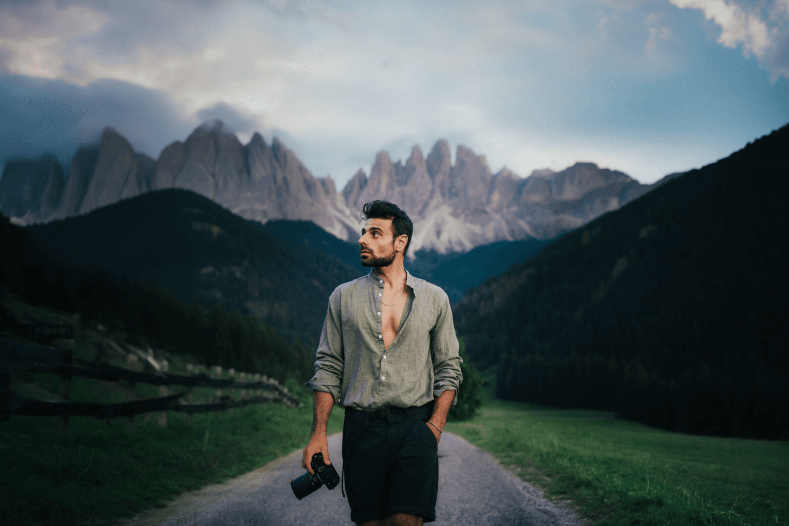 A person stands against a vibrant background of orange and yellow wavy patterns. They are wearing a dark coat, looking contemplative and thoughtful.