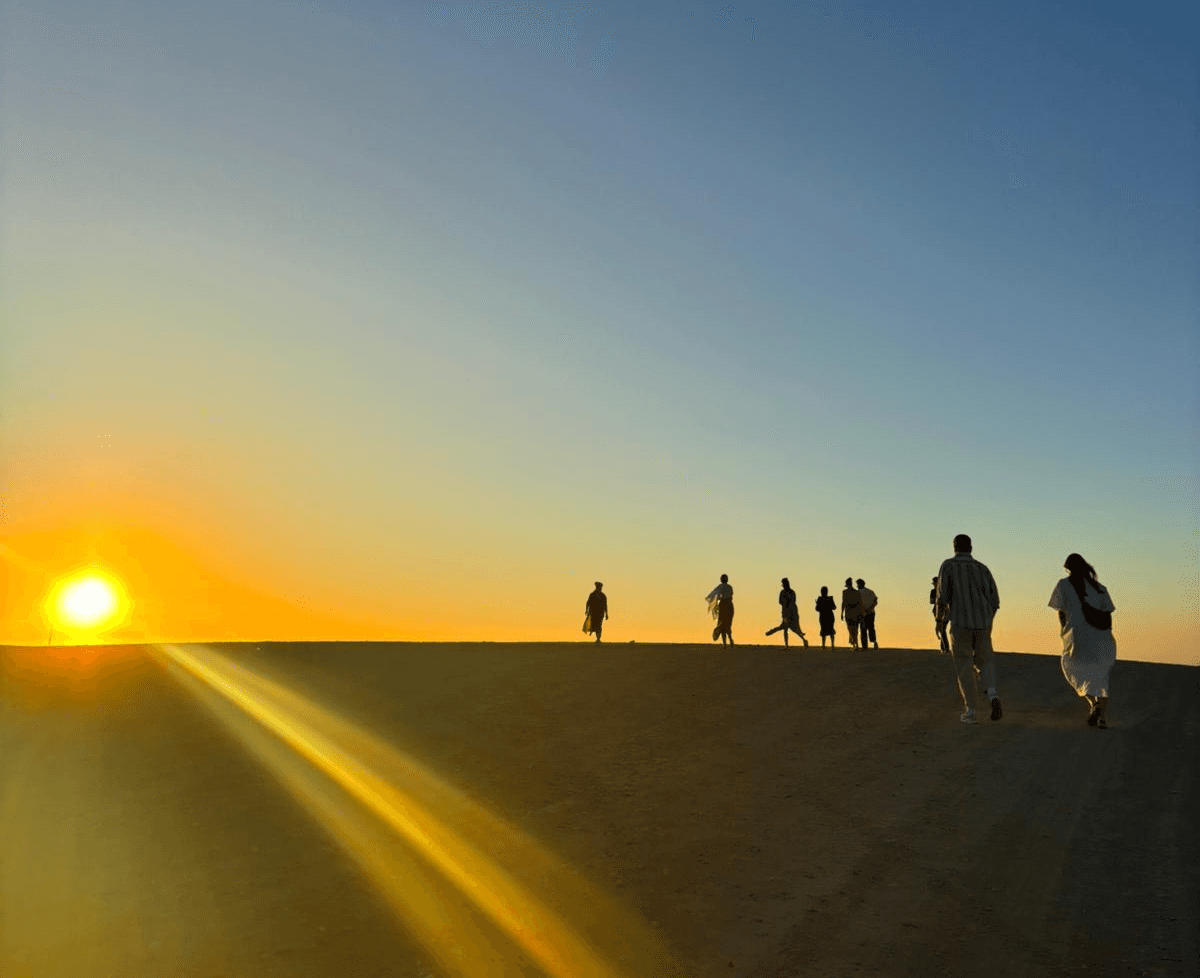 Team walking over the horizon of the desert at sunset