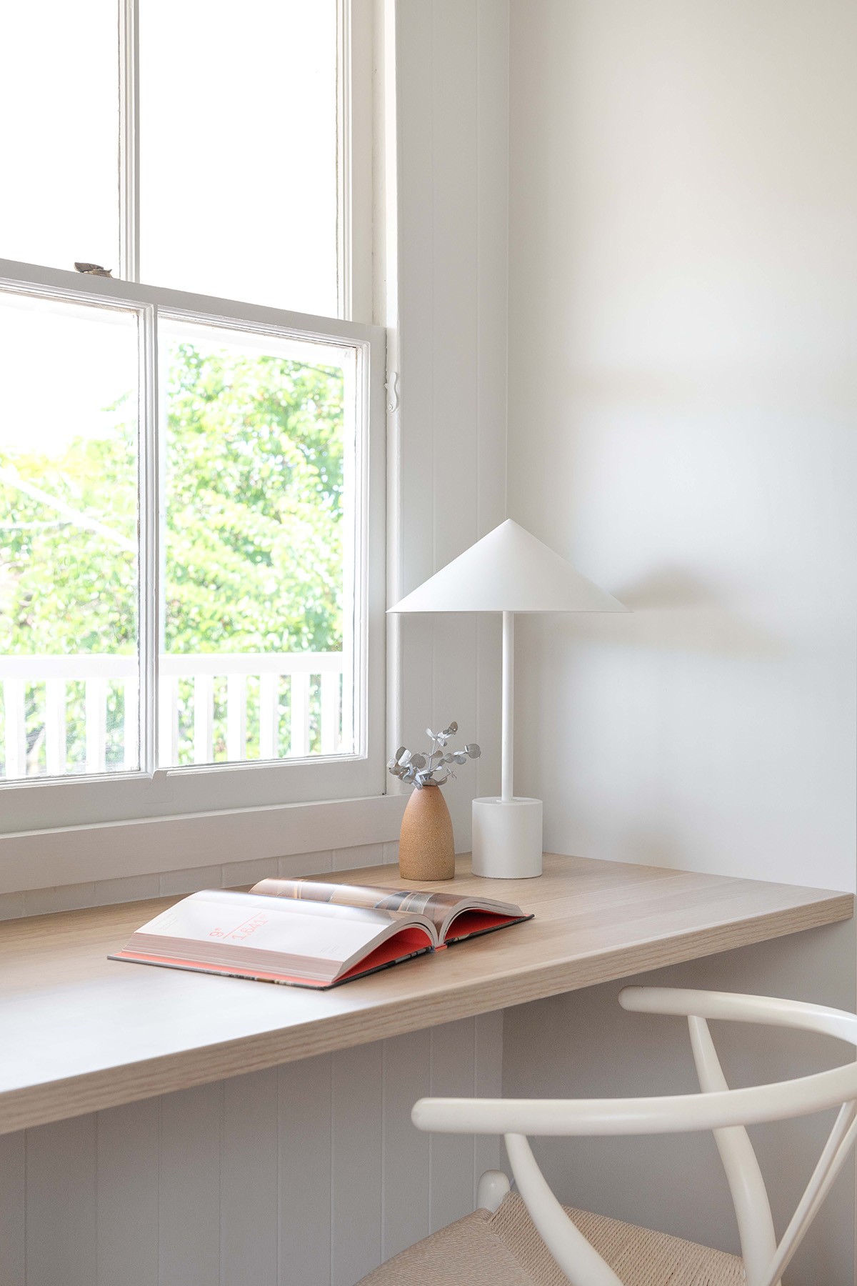 Window-side study nook at The Stables, featuring timber surfaces, minimal furnishings, and views into the surrounding greenery.