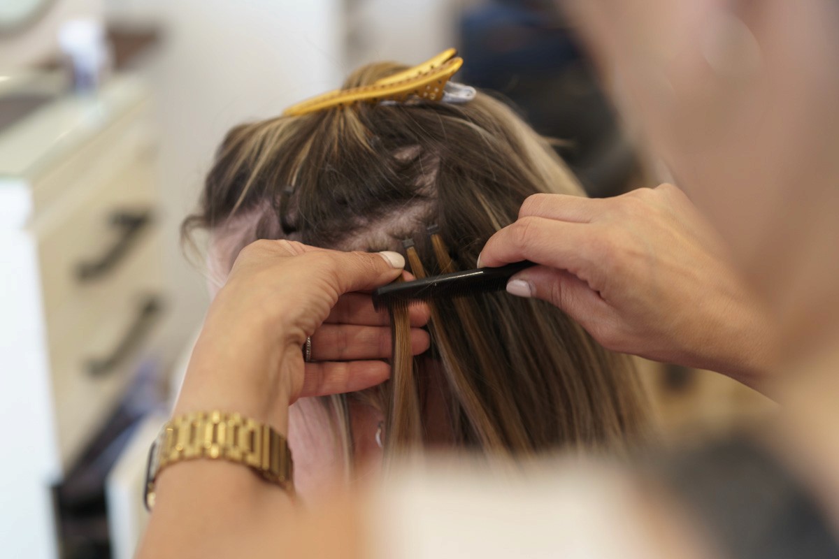 Close-up of a stylist applying hand-tied extensions to blonde hair, showing sectioning and precision during the extension installation process.