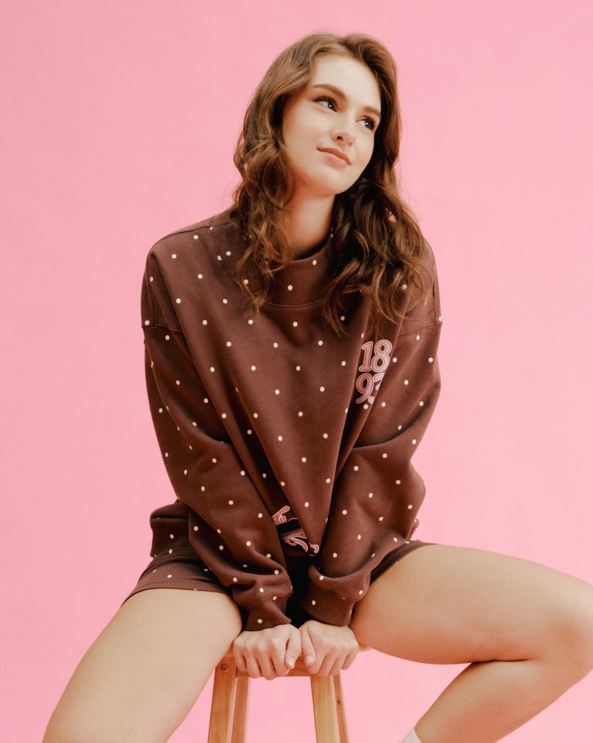 Model wearing a chocolate-brown sorority sweatshirt and shorts decorated with small white polka dots.