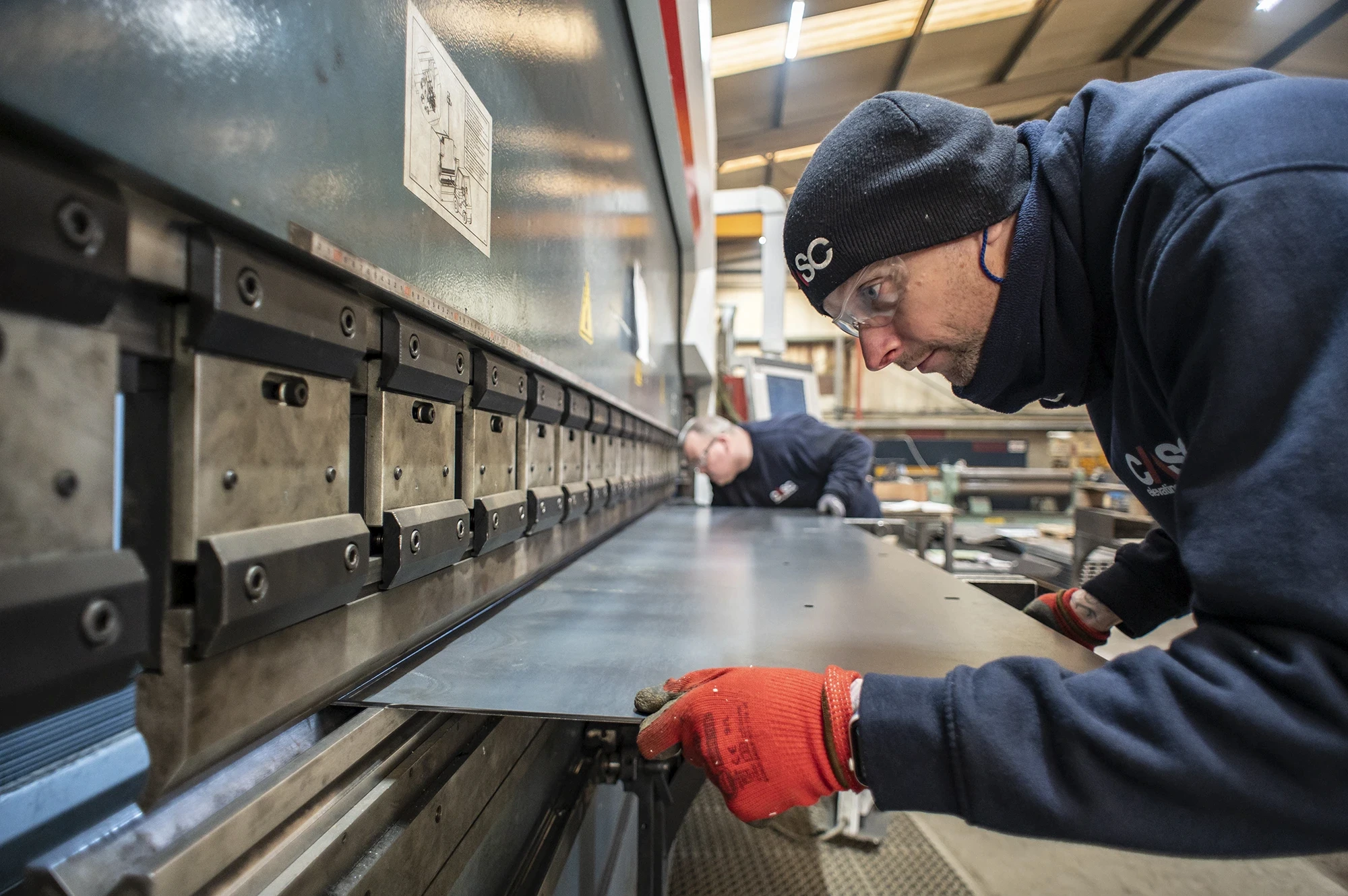 Worker operating a metal folding machine to bend a steel sheet inside CASC’s fabrication workshop.