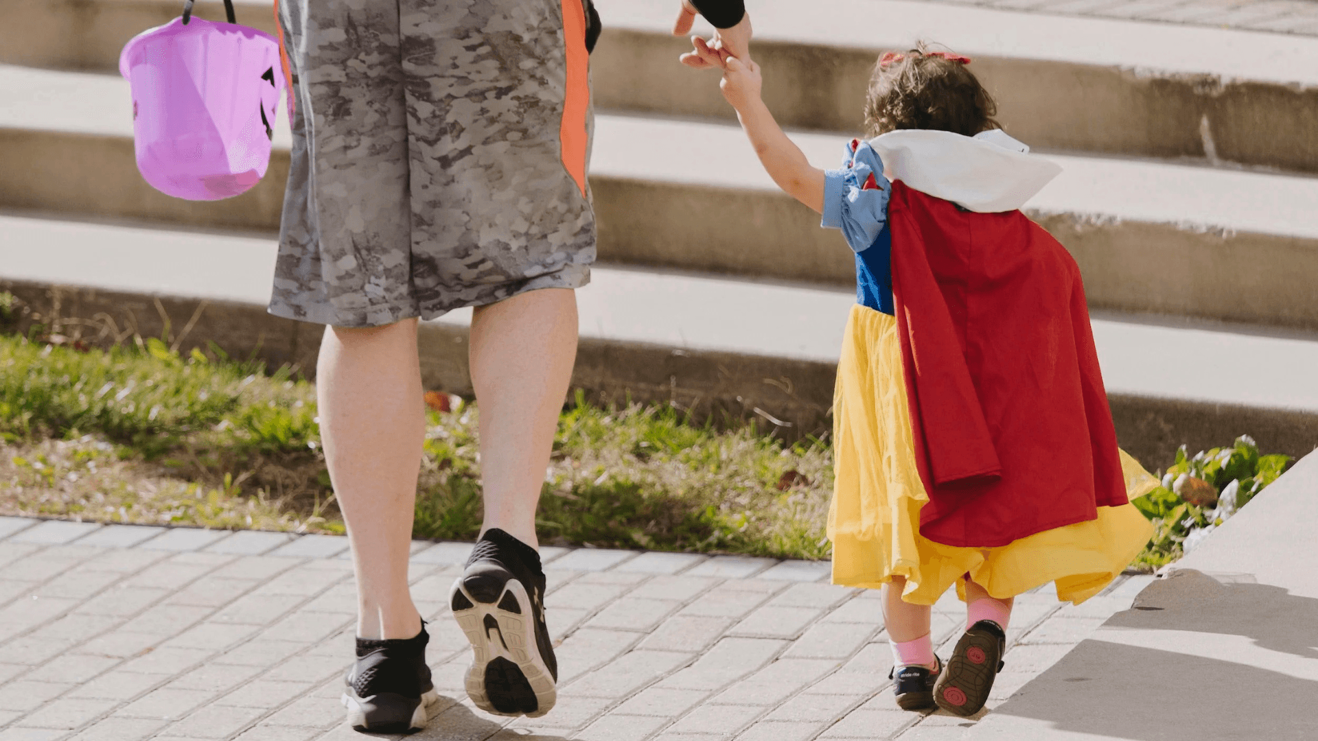 A closely cropped photo of a young child dressed as snow white holds hands with an adult figure who is cropped at the hips
